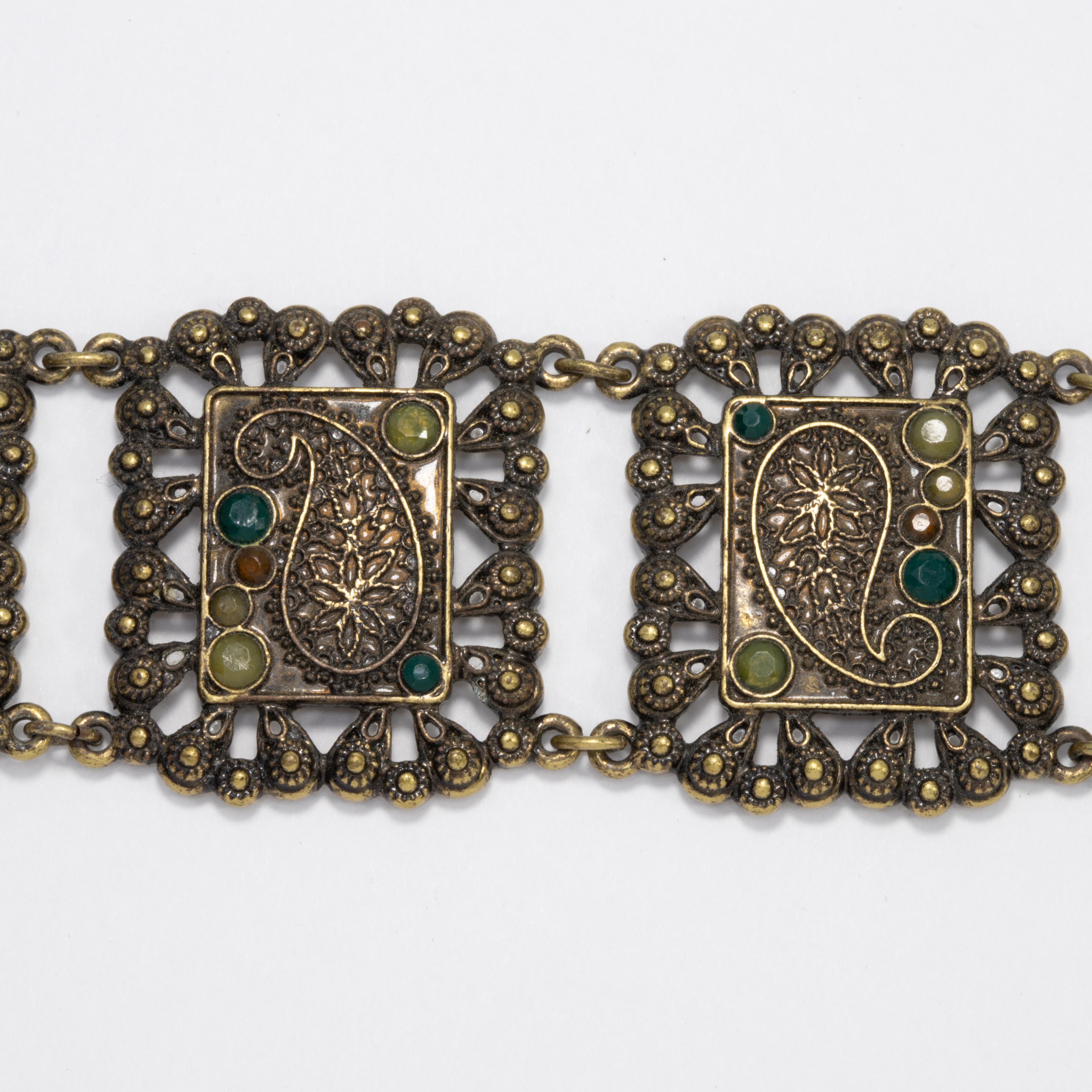 Un exquis bracelet vintage, avec des maillons décoratifs aux motifs paisley, rehaussés de cristaux d'olivine et d'émeraude.

En laiton. Fermeture par un fermoir à bascule.