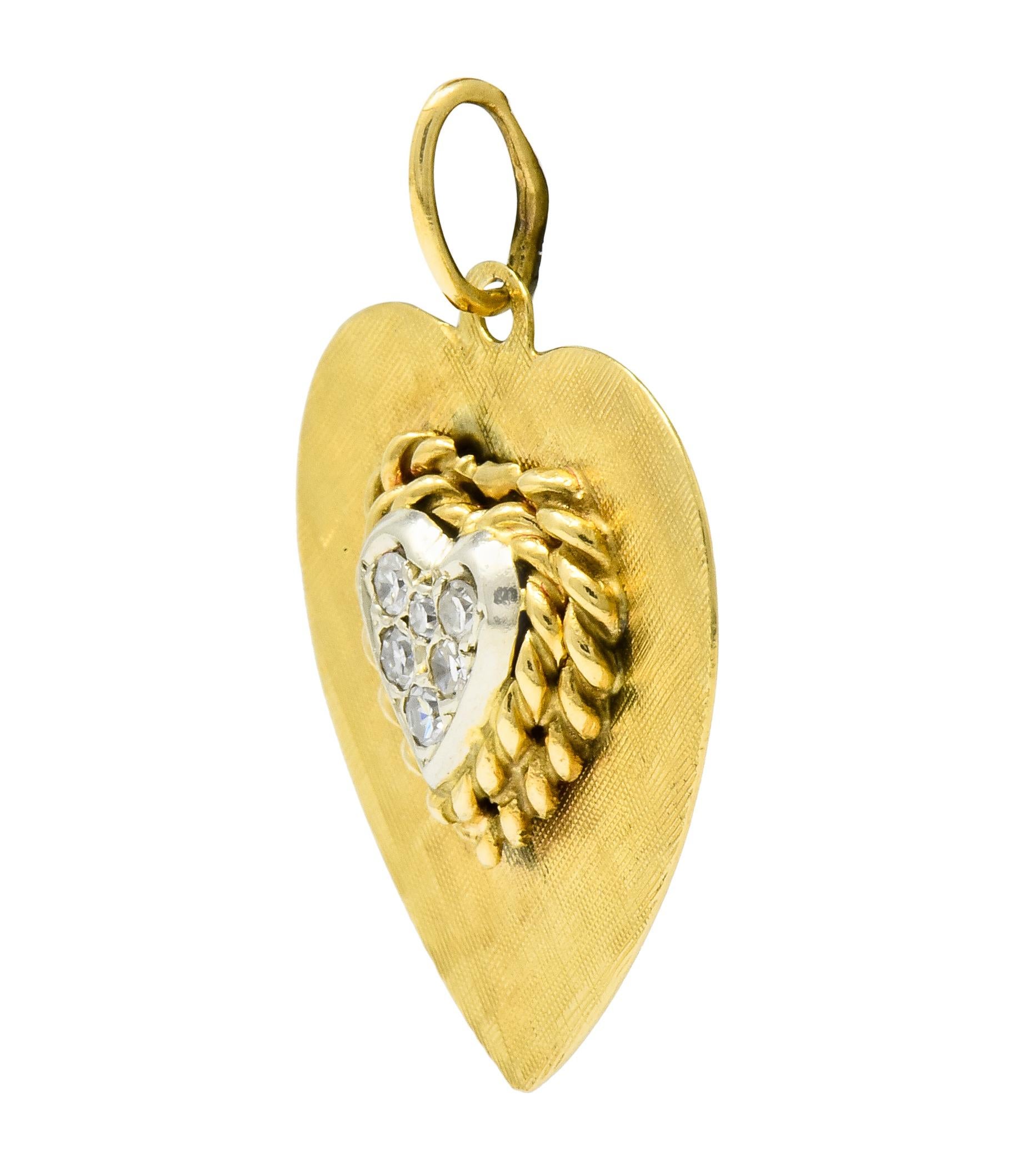 Designed as a gold heart charm with a cross hatched finish

Centering a platinum heart center pavé set with single cut diamonds weighing in total approximately 0.18 carat; eye-clean and white

Surrounded by gold twisted rope motif

With maker's mark