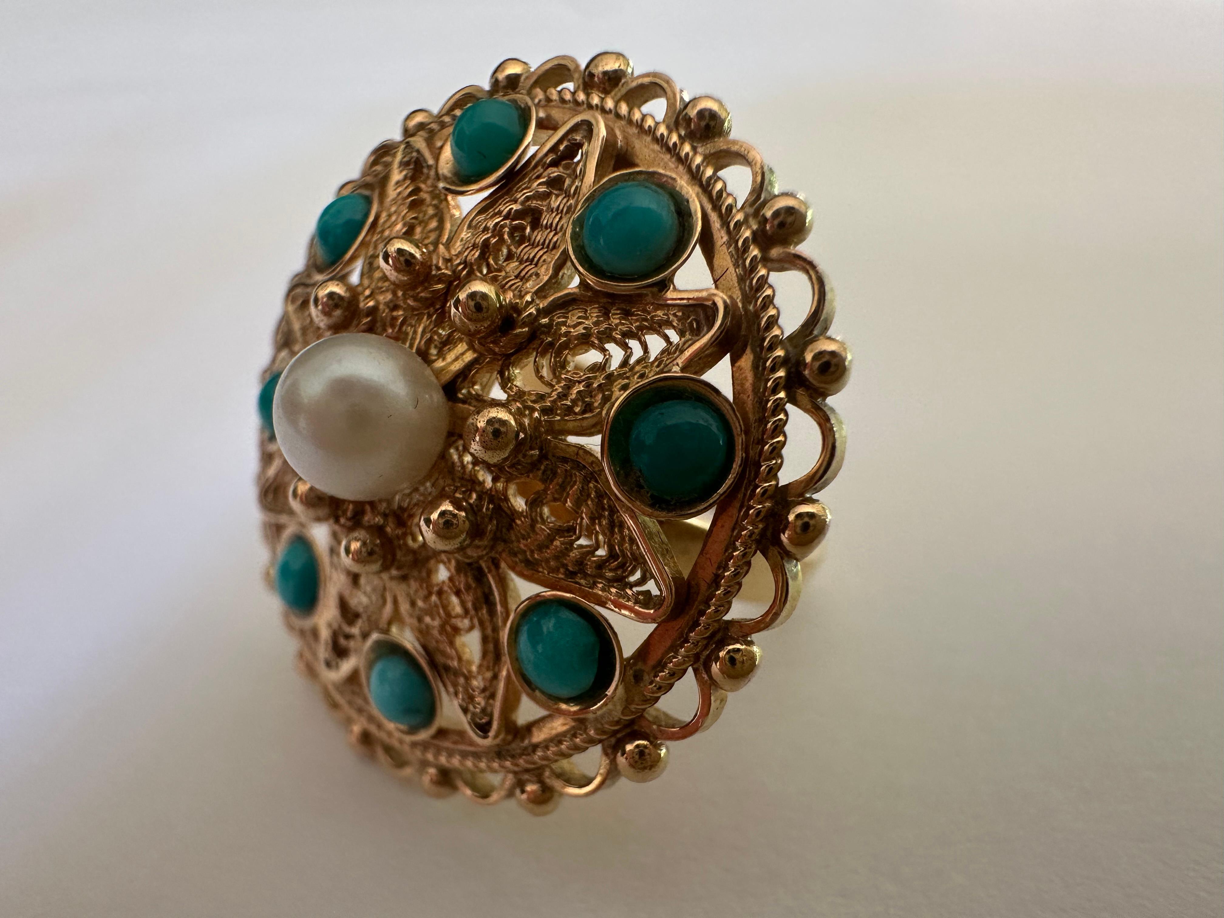 Fabriqué dans les années 1960, ce bijou du milieu du siècle présente une perle blanche en son centre, entourée de huit cabochons ronds de turquoise persane naturelle, le tout serti dans une monture complexe en or jaune 14 carats. 