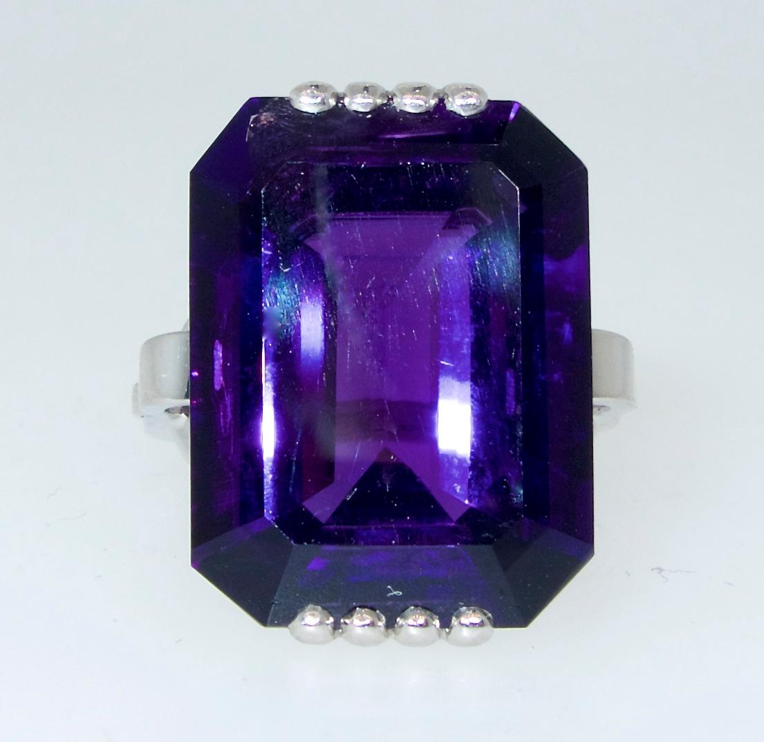 The center emerald cut amethyst is very fine with a deep purple red color.  This vivid clear center stone is set in an unusual hand made setting.   It is now a size 6 and can easily be sized.  Probably American, circa 1950.
