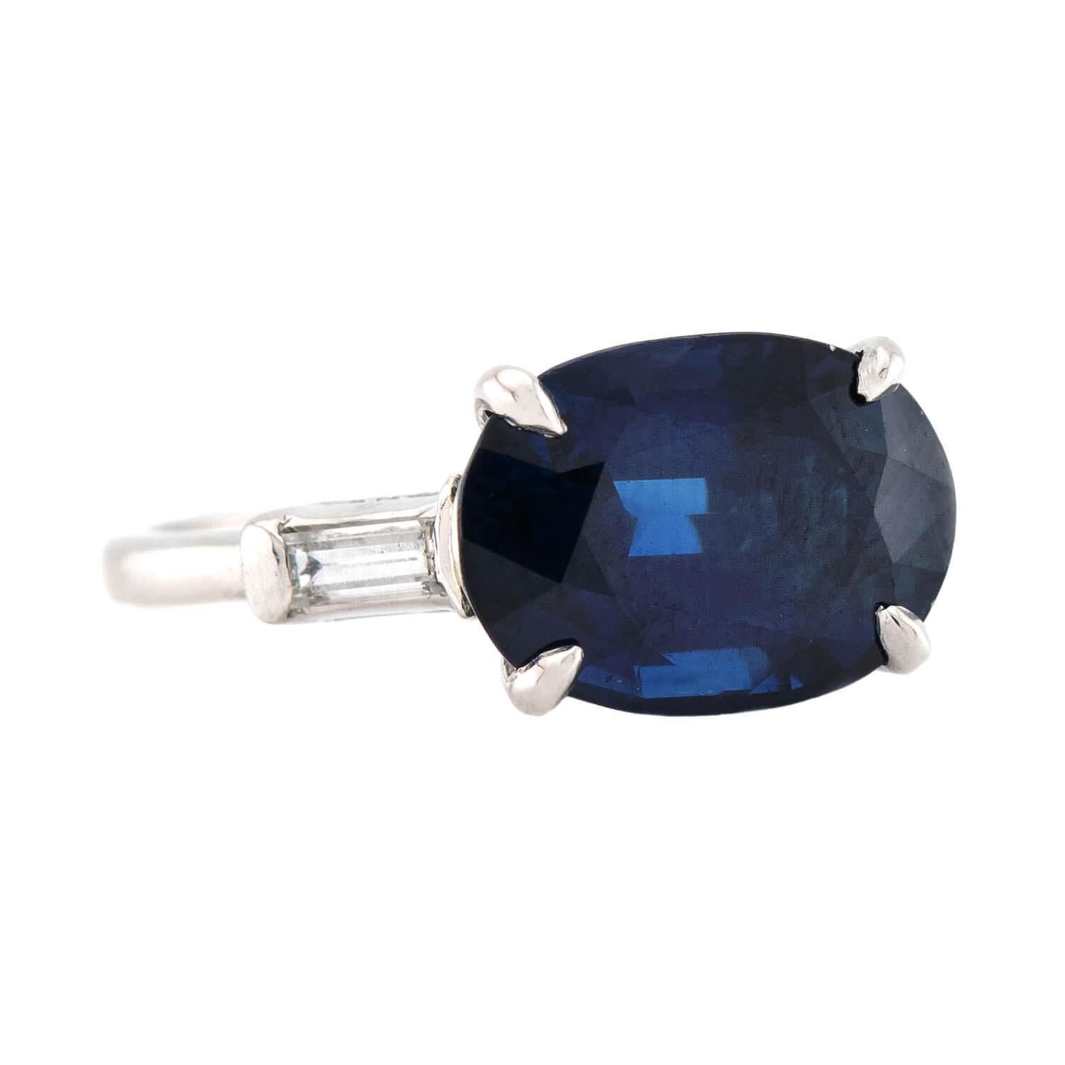 An absolutely breathtaking sapphire and diamond engagement ring from the Retro (ca1950s) era! This beautiful piece is crafted in platinum and features a horizontally-set 6ct oval cut sapphire. The sapphire is held within a four prong-setting, and