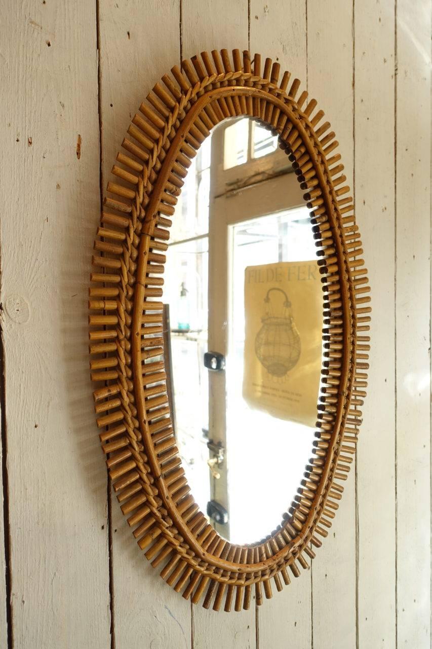 Wonderful vintage midcentury oval French rattan or wicker mirror. With its original glass and gorgeous 'sunbeam' wicker pattern frame. Hand weaved in a stylish fashion, circa 1950s. Super decorative and spot on for today’s interior tendencies. Shiny