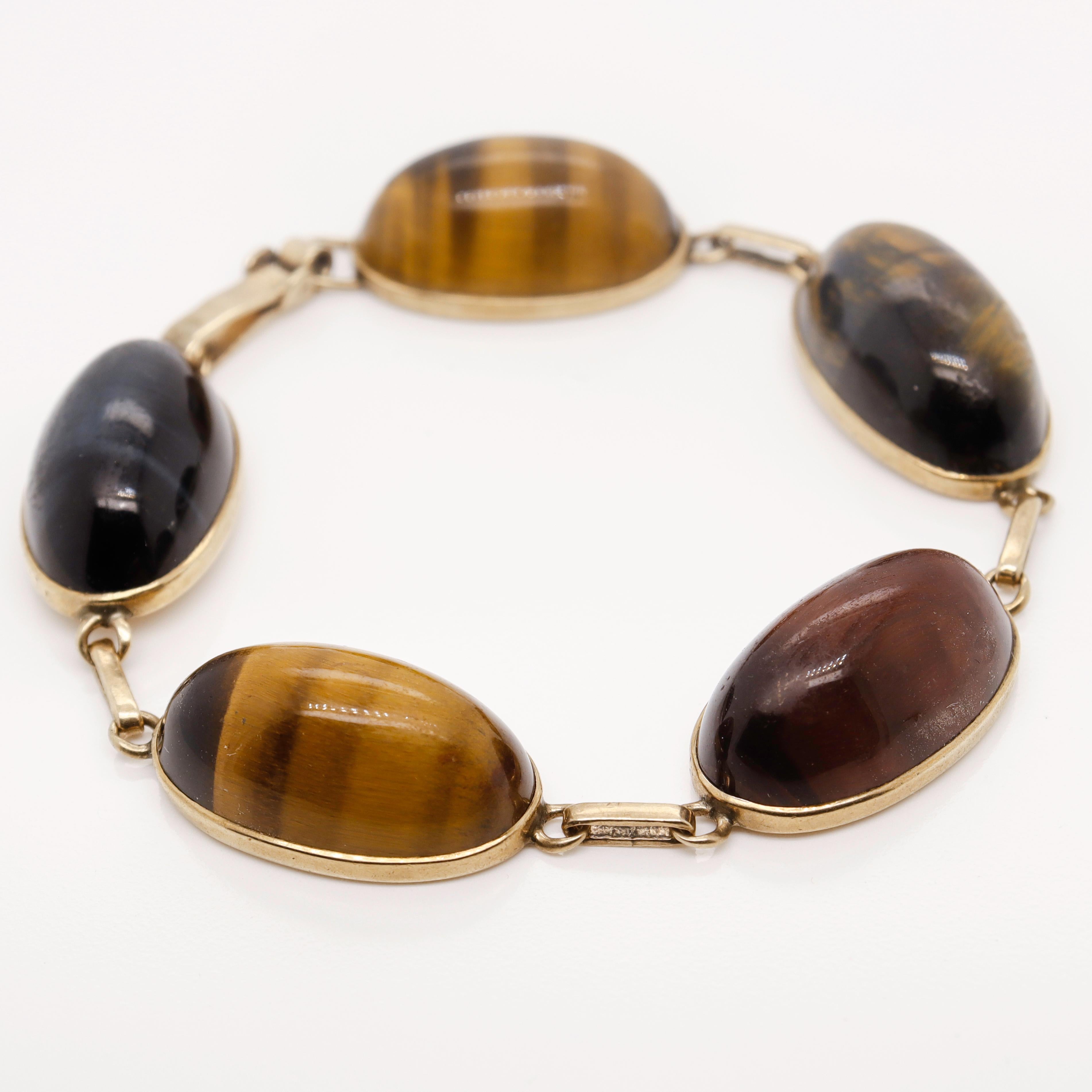 Ein feines, retro Tigerauge & Gold Armband.

Aus 9-karätigem Gold.

Mit glatten ovalen Gold Tigerauge, Drachenauge (rote Tigerauge), & Hawk's Eye (blaue Tigerauge) Cabochons in 9ct Gold Lünetten gesetzt und mit flachen Kabel Links verbunden. 