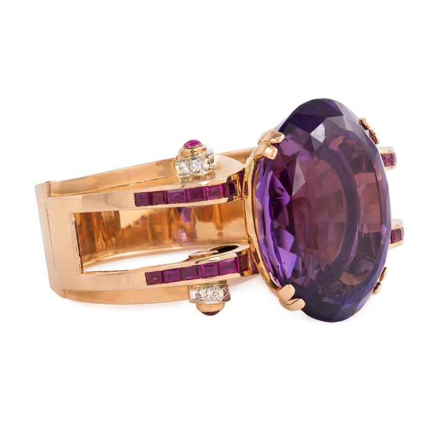 A Retro rose gold bangle bracelet centering on a large oval amethyst, with open scrolled shoulders set with calibré rubies and accented on the sides with diamonds and cabochon rubies, in 14k.

Inner circumference: 6 3/4