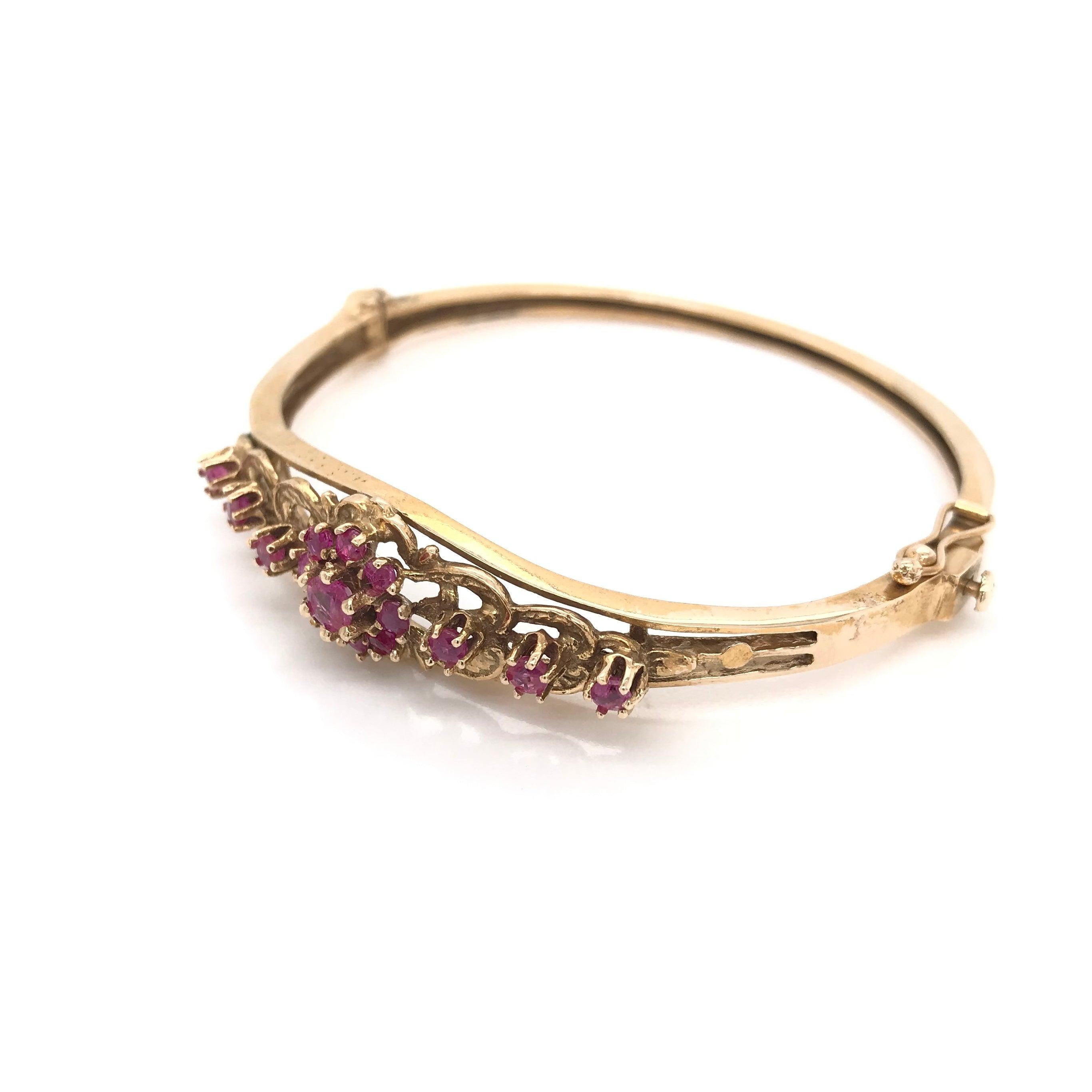 This retro ruby and gold bangle was crafted sometime during the Mid Century design period (1940-1960). Rubies were the gemstone darling of the retro design period; This 14k gold bangle features 15 round rubies set in a lovely floral motif.