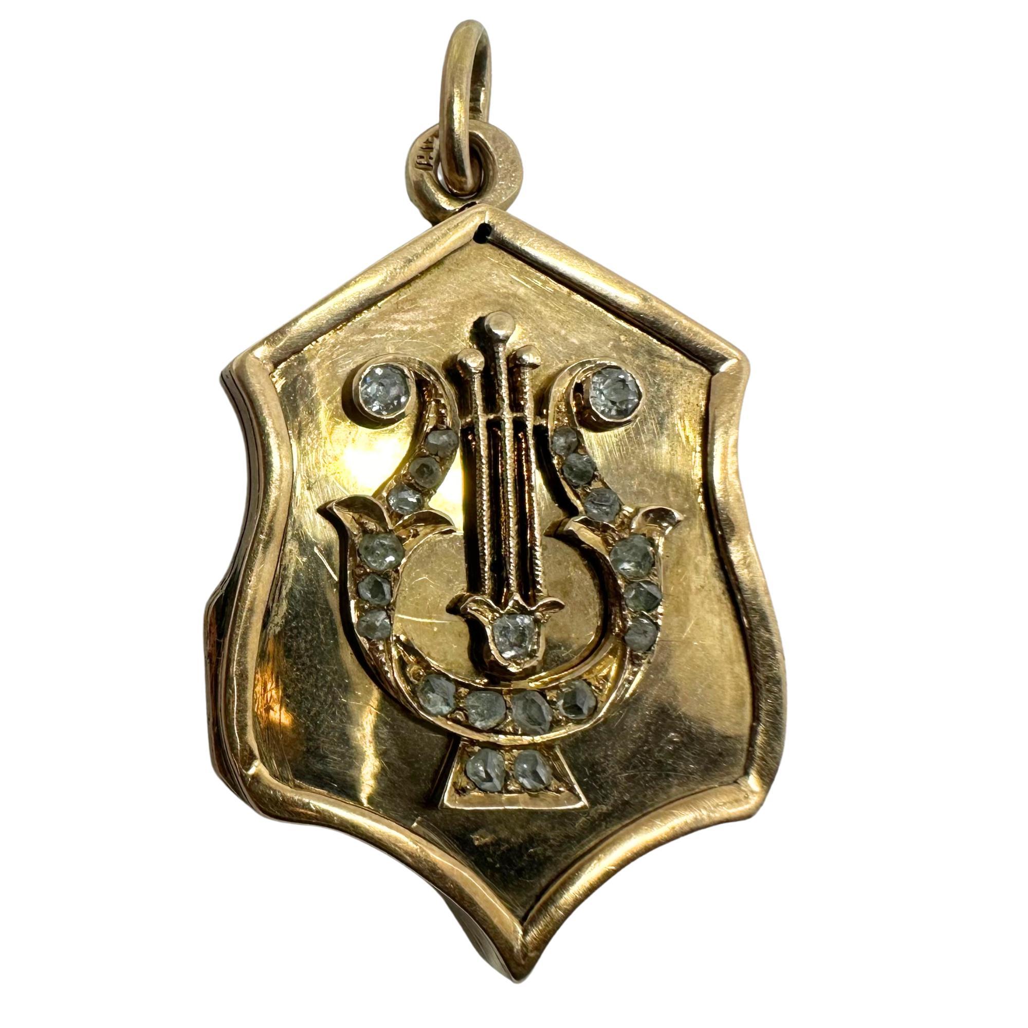 Vintage Russian locket made of solid 14K rose gold, shaped like a shield and decorated with a raised lyre design. The lyre, a symbol of music, is set with about 0.50 carats of rose-cut diamonds. The piece opens to hold a small photo or