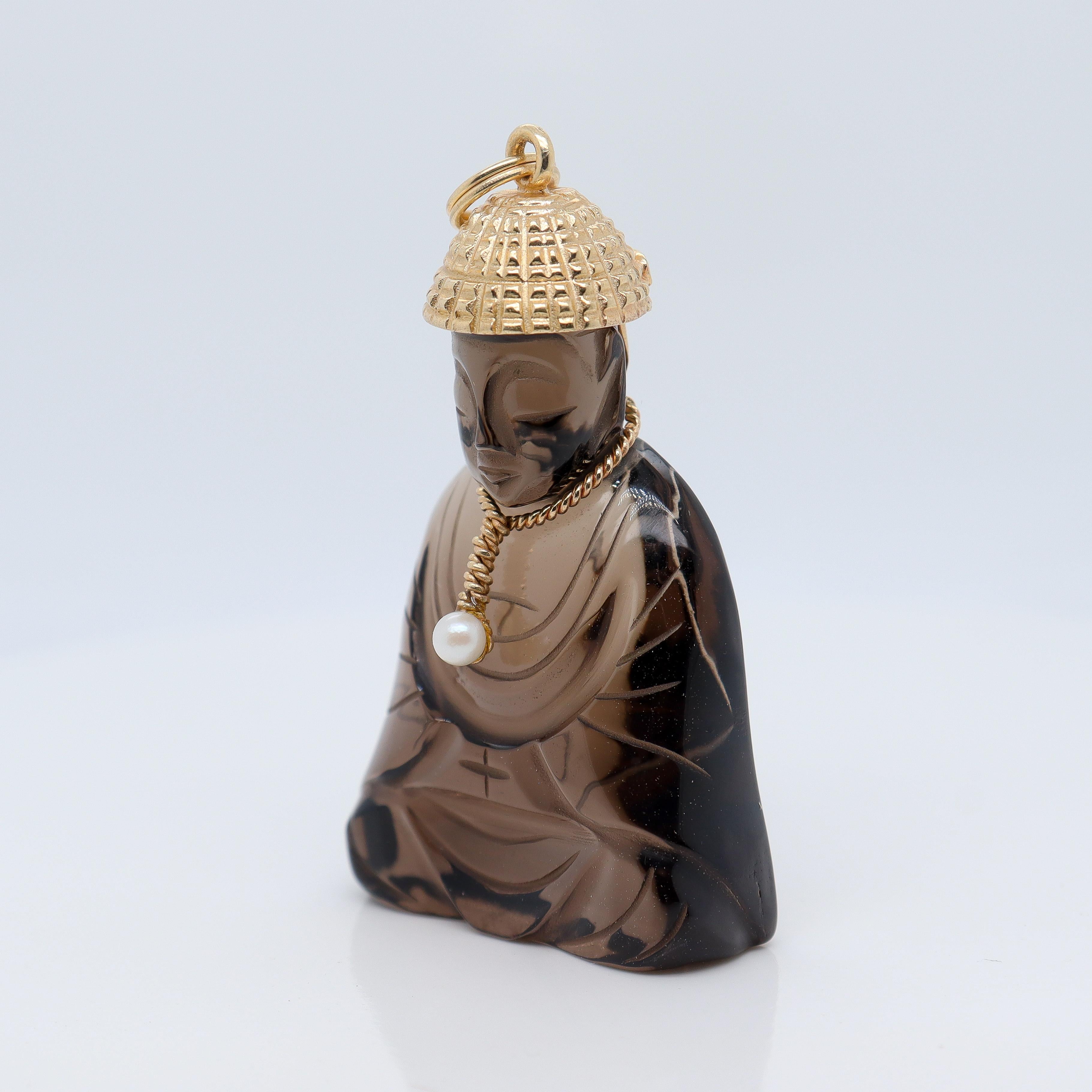 A fine retro gold, smoky quartz, and seed pearl pendant.

In 14K gold.

By the American Charm Co. 

In the form of a seated stylized Chinese Buddha. The body consisting of carved smoky quartz, the hat and necklace of gold, and the pendant of the