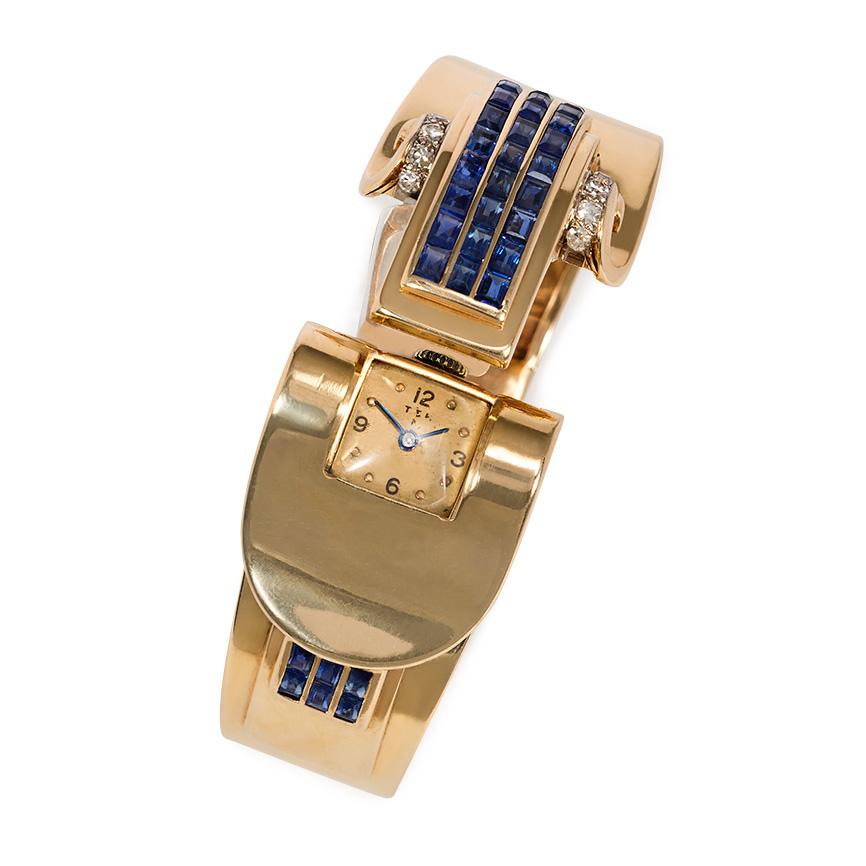 A Retro gold and channel-set sapphire bracelet watch of overlapping scrolled design with diamond embellishment, in 14k.  Atw 0.40 ct. single cut diamonds; approximately 5.00 cts. tw sapphires.  Trabert & Hoeffer Mauboussin.  Inner circumference