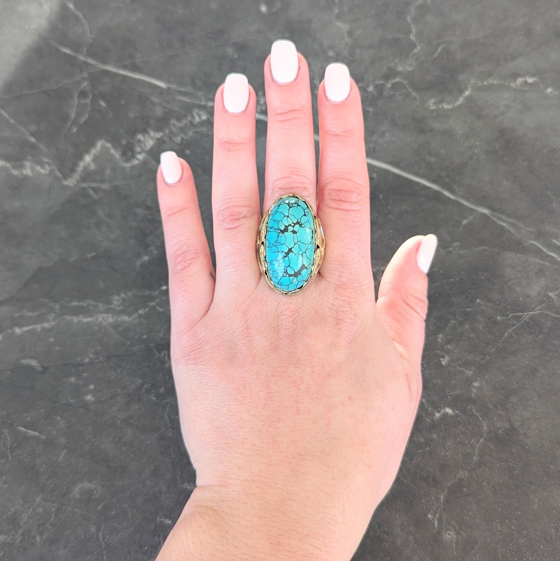 Centering an oval shaped turquoise cabochon measuring 17.0 x 32.0 mm
Opaque light blue to bluish green in color with veining brown matrix
Set in a scalloped bezel with grooved geometric decoration
Flanked by shoulders with fanning 22 karat gold