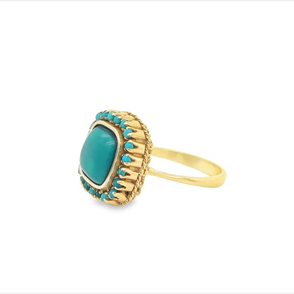 One fantastic design crafted in 18k yellow gold. The ring highlights one cabochon cut turquoise gemstone that is accented with turquoise gemstones in a halo setting. The color of the turquoise gemstones is beautiful, highlighting various color tones