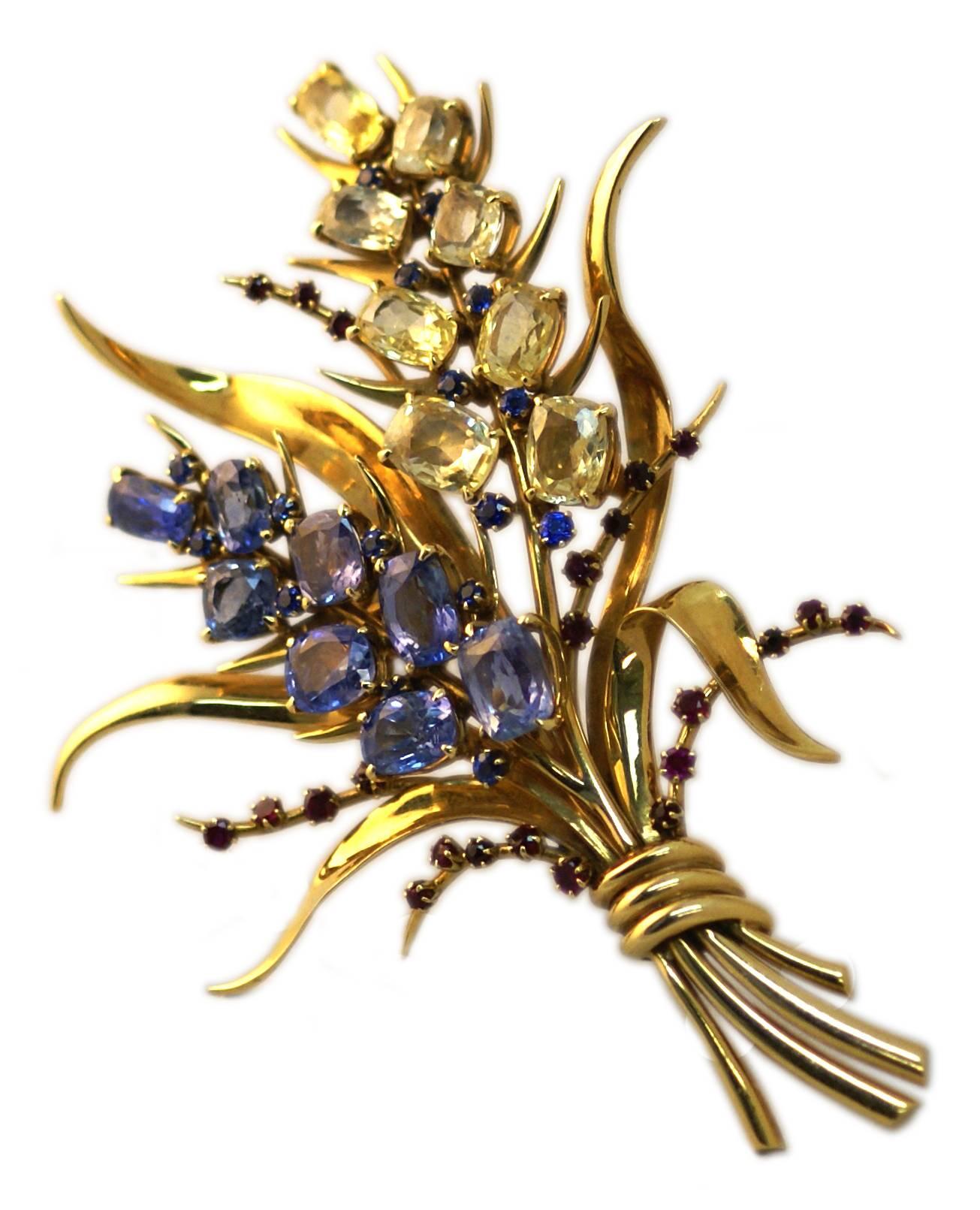 A brooch designed as a sculpted 18k gold bouquet, the two blossoms centering upon either a circular-cut ruby or sapphire cluster pistil, extending elongated cushion-cut blue or yellow sapphire petals, enhanced by circular-cut ruby and sapphire buds,