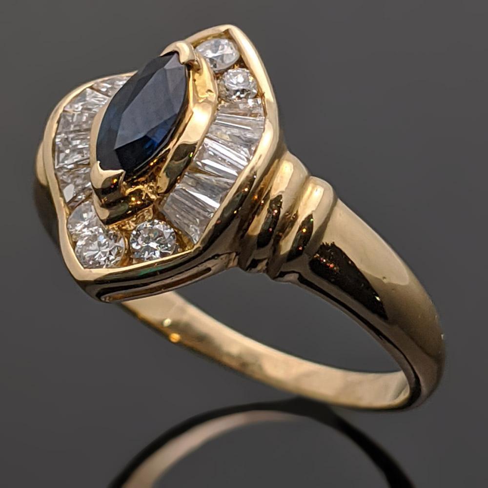 A vintage 14kt yellow gold ring featuring a blue marquis cut sapphire at an estimated weight of 0.16ct. The sapphire is surrounded by round diamonds as well as baguettes that have an estimated 0.42cttw. Estimated weight of gold is 3 gr. 

We will