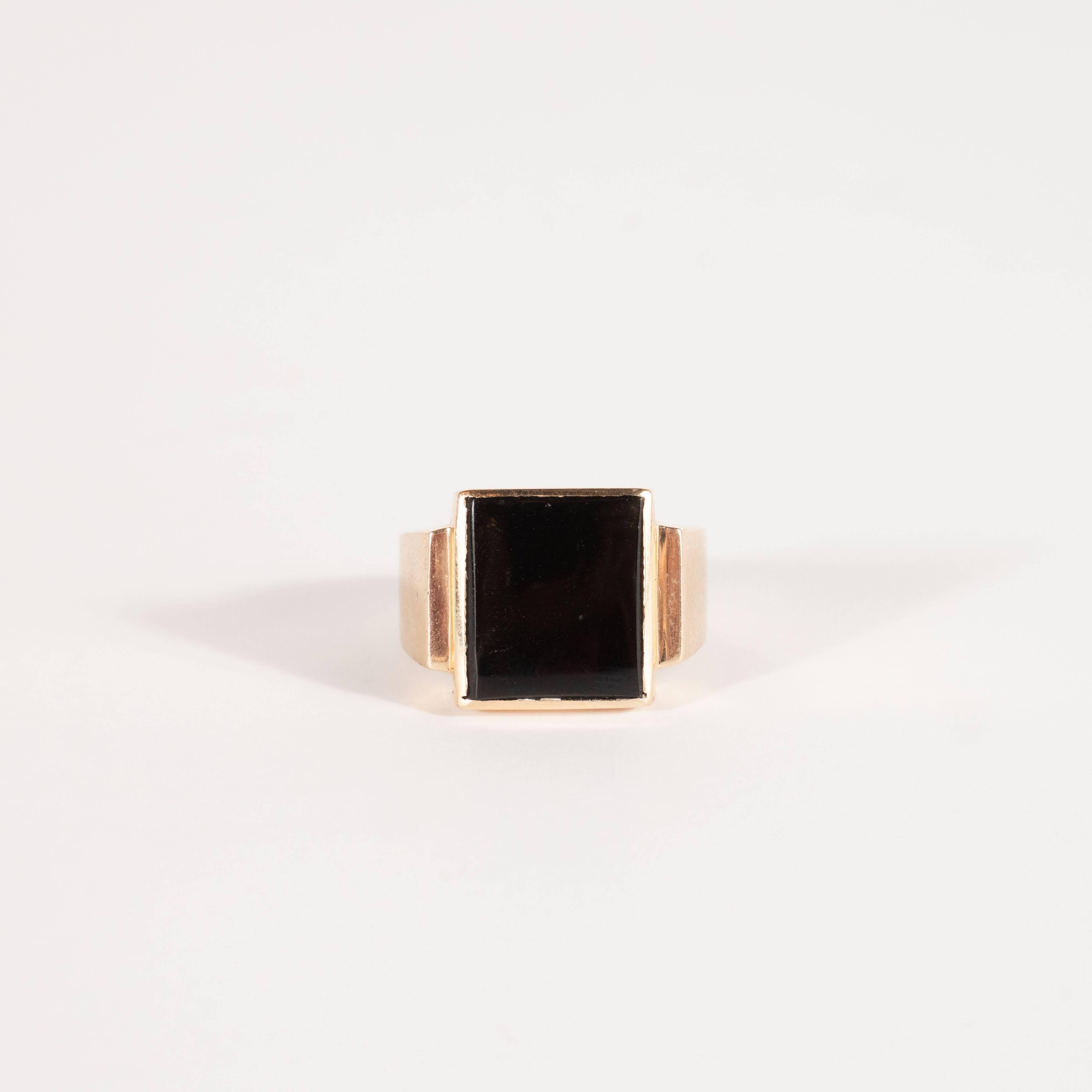 This handsome and refined ring was realized in the United States, circa 1940. It features a rectangular black onyx insert with skyscraper style sides consisting of two tiers of 14kt yellow gold, the bottom of which descends into the tapered band.