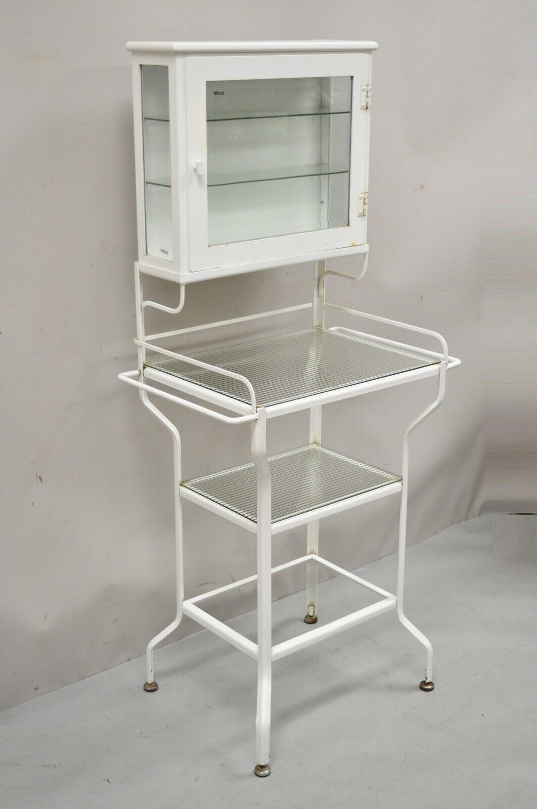 Retro vintage style Industrial metal white bathroom cabinet vanity stand. Item features upper swing door with 2 glass shelves, towel rods to sides,3 lower tiers with 2 glass shelves, Iron metal frame. Circa late 20th - early 21st century.