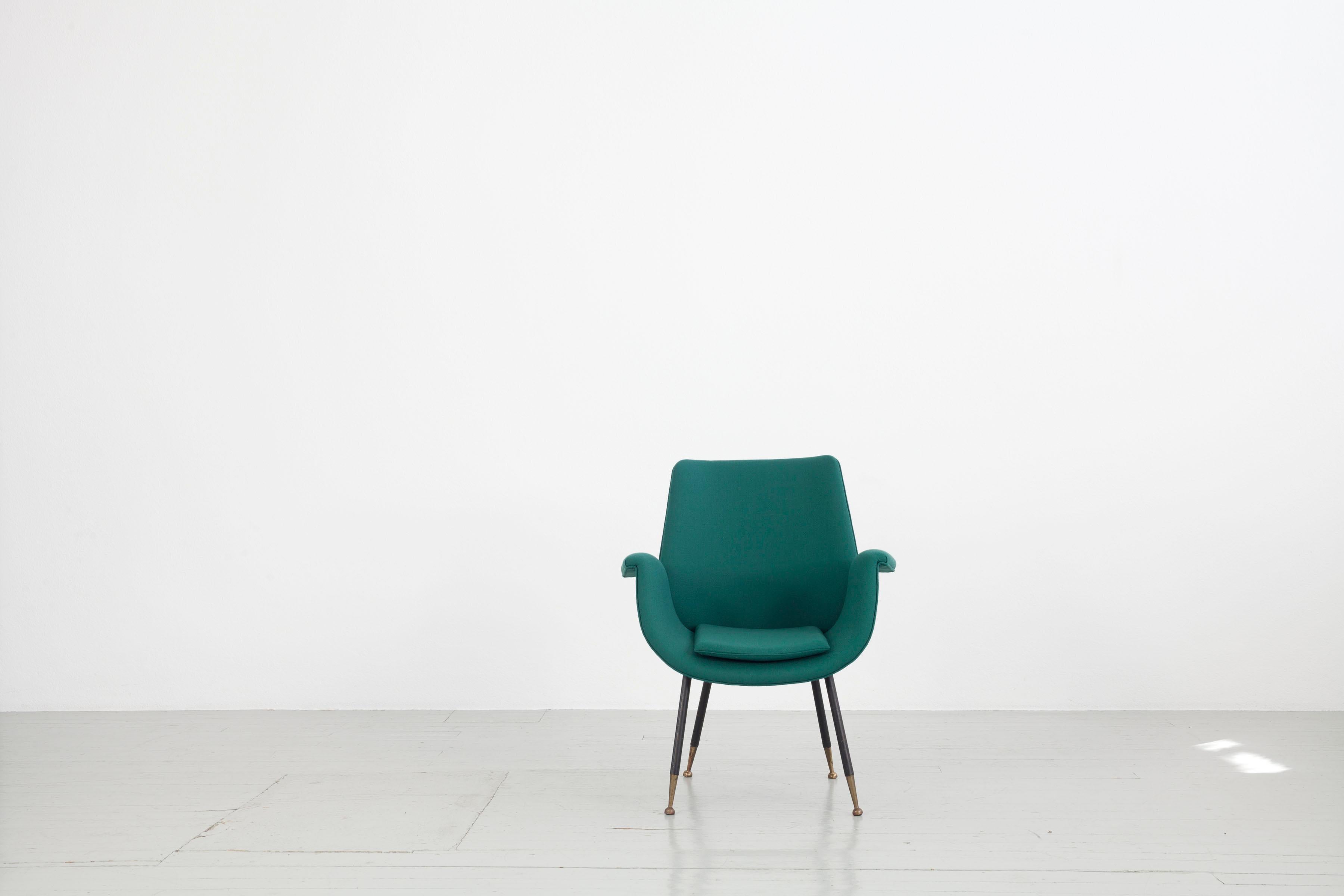 This Italian armchair was designed by Gastoni Rinaldi in the 1950s. The rounded seat and the thin iron legs with brass ends give the piece of furniture elegance. The armchair has been reupholstered by us and covered with petrol-coloured Kvadrat