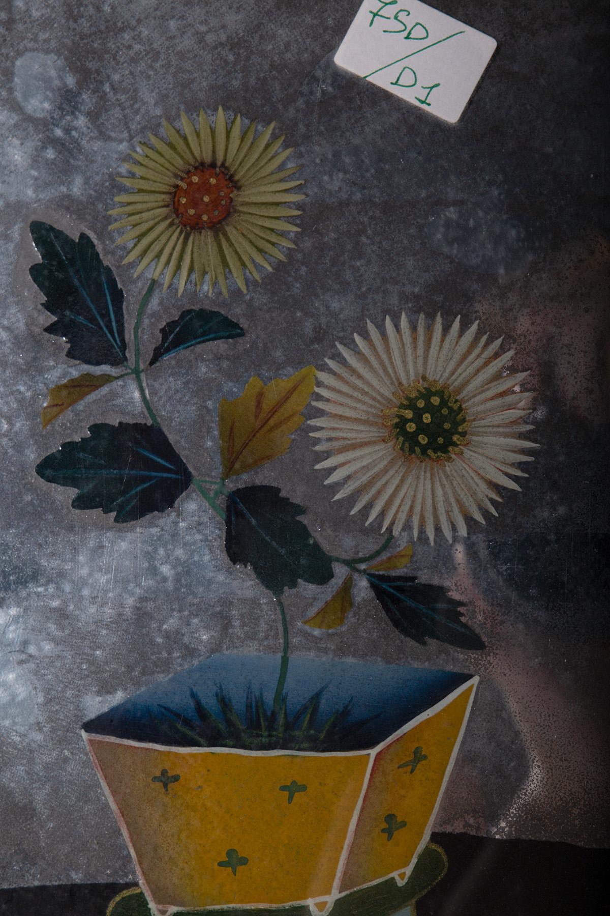 Cette peinture sur verre inversé, créée en Chine au début des années 1800, incarne la délicatesse et l'élégance typiques de l'artisanat oriental. Au centre de la pièce, deux fleurs ressemblant à des chrysanthèmes s'épanouissent gracieusement dans un