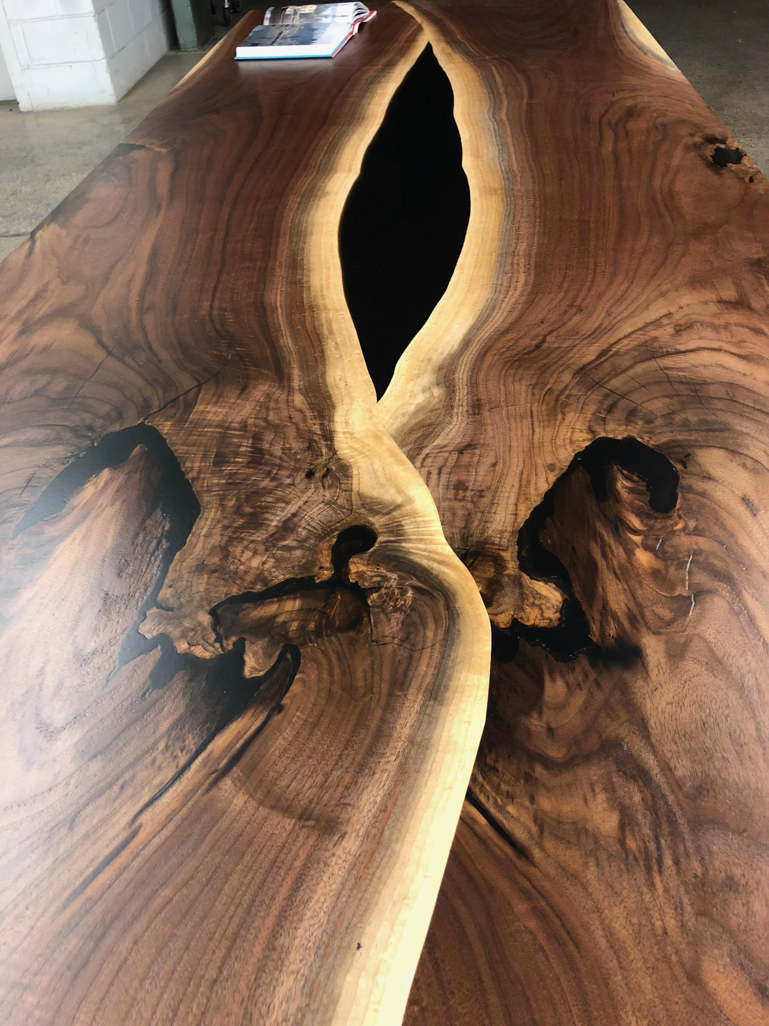 A bookmatched set of walnut slabs done in an overlaping style where one end overlaps the other in a sort of circular manner. The void in the middle is filled with a tinted resin, lucite legs and the precision of the raw edge overlapping with the