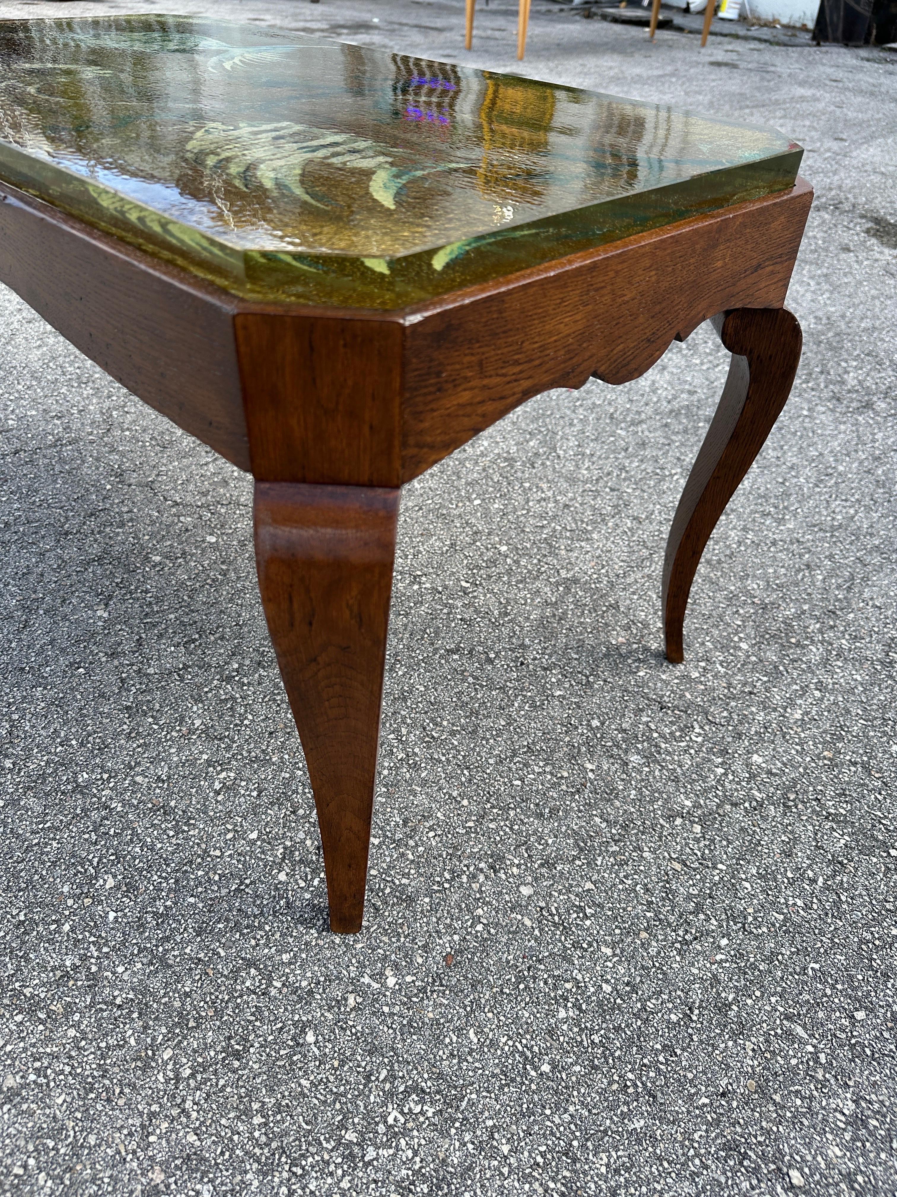 Beautifully reverse painted thick glass top with an aquarium scene in tones of gold, blues and greens. Art Deco mahogany wood base is rich with color and features scalloped edges and cabriolet legs. Very much in the style of René Prou.  THIS ITEM IS