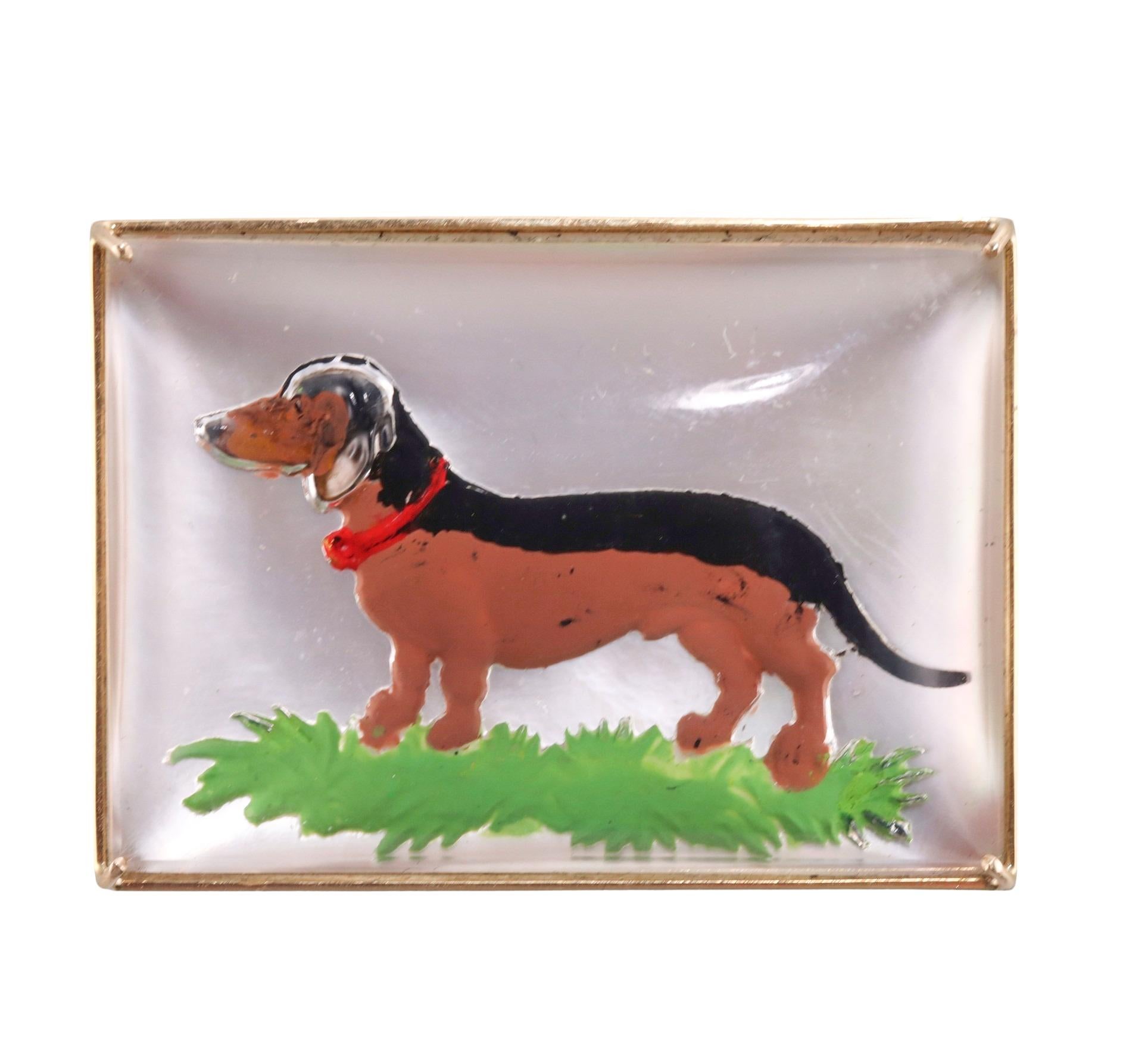 14k gold brooch, depicting a Dachshund dog, set in crystal reverse painting, backed with mother of pearl. The brooch measures 44mm x 32mm, and weighs 36.6 grams. Tested 14k, not hallmarked.