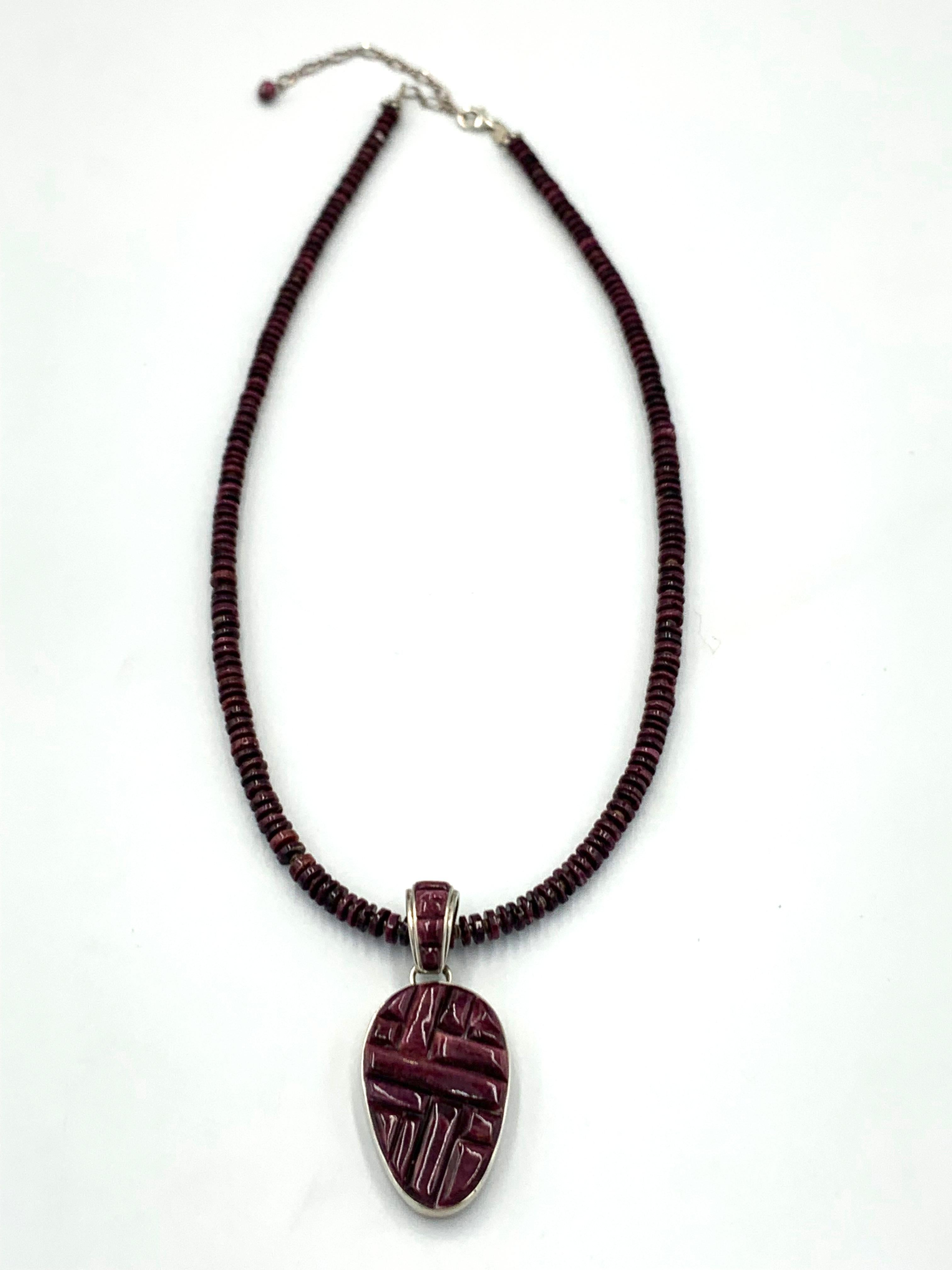 Ciondolo reversibile dell'argentiere Navajo Calvin Begay. Il ciondolo a forma di ostrica spinosa viola con intarsio di ciottoli è incastonato in argento sterling. Il retro è in argento sterling con un motivo tradizionale. Il ciondolo da 7/8