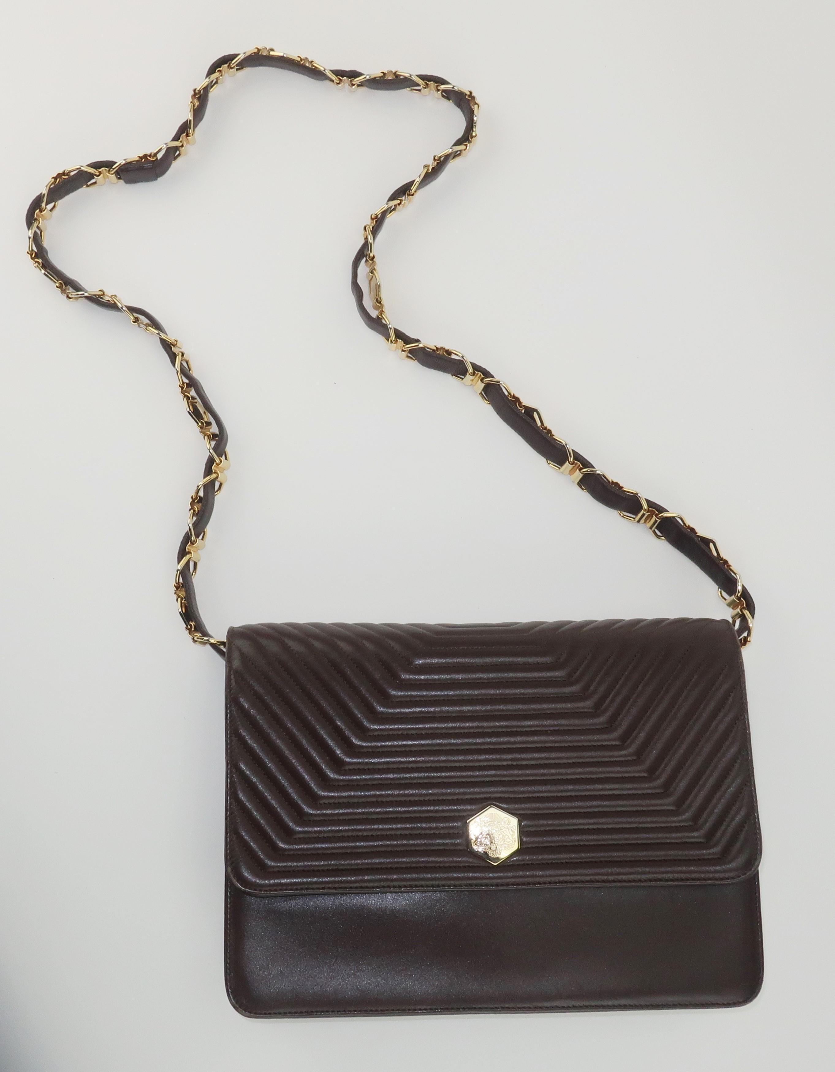 Vintage brown channeled leather handbag with a gold tone chain enhanced leather shoulder strap by French design house, Revillon.  The fold over envelope style bag has a snap closure embellished by a gold tone logo medallion which opens to reveal a