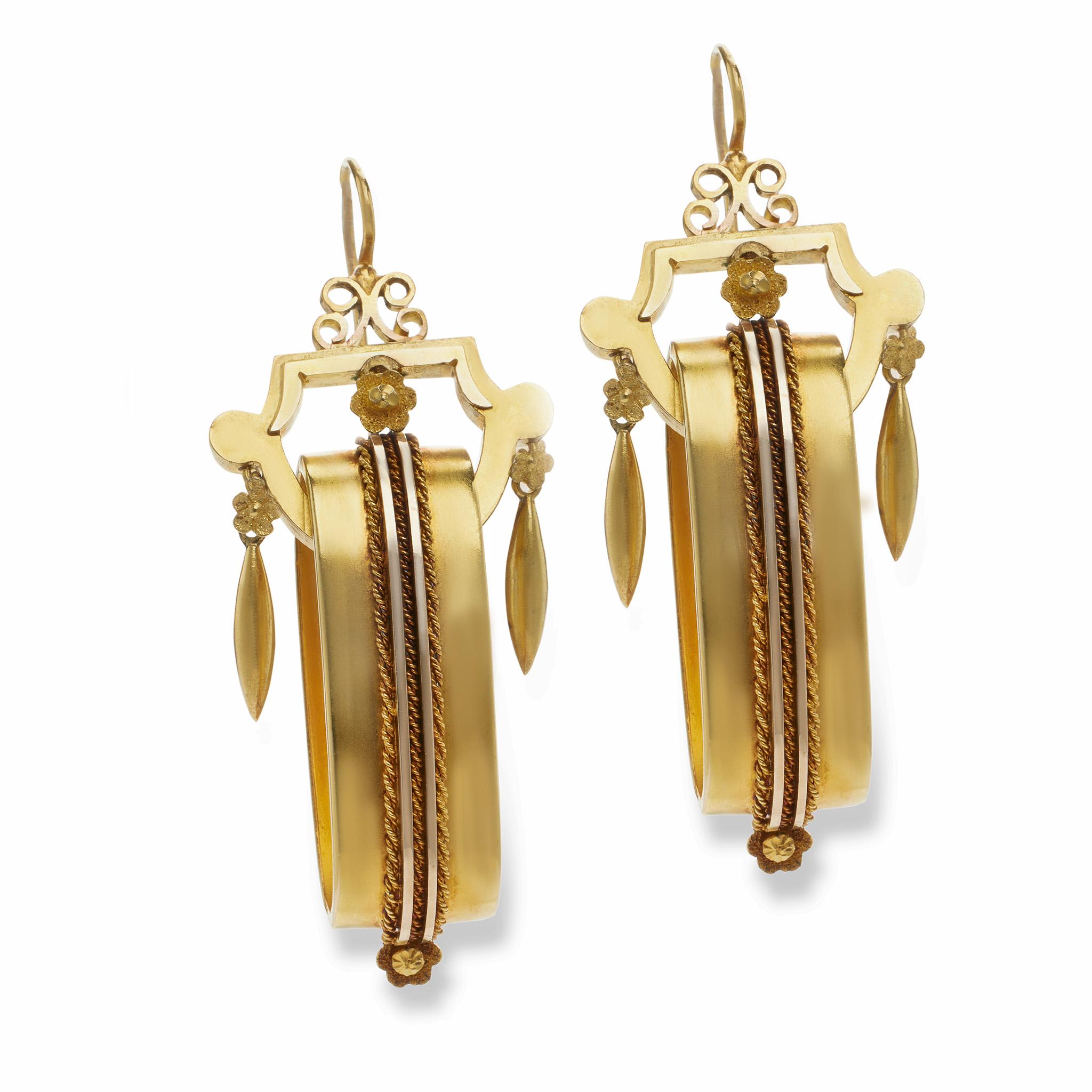 Likely made in England in the 1860s-70s, these 15k gold earrings were created in the Revival style. Each pendant earrings is designed as a geometric scrolling top suspending a freely-set central elongated ring with vertical double line motif and