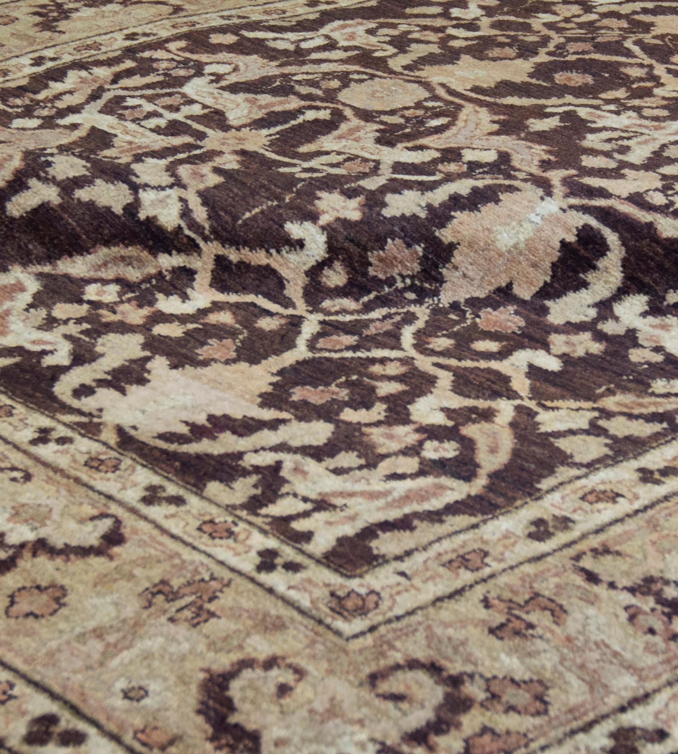 Questo tappeto di ispirazione indiana Agra, tessuto a mano, presenta un campo marrone scuro con un invitante campo Garrus, con un bordo a palmette intrecciate beige tenue, tra delicate strisce di viti floreali avorio.