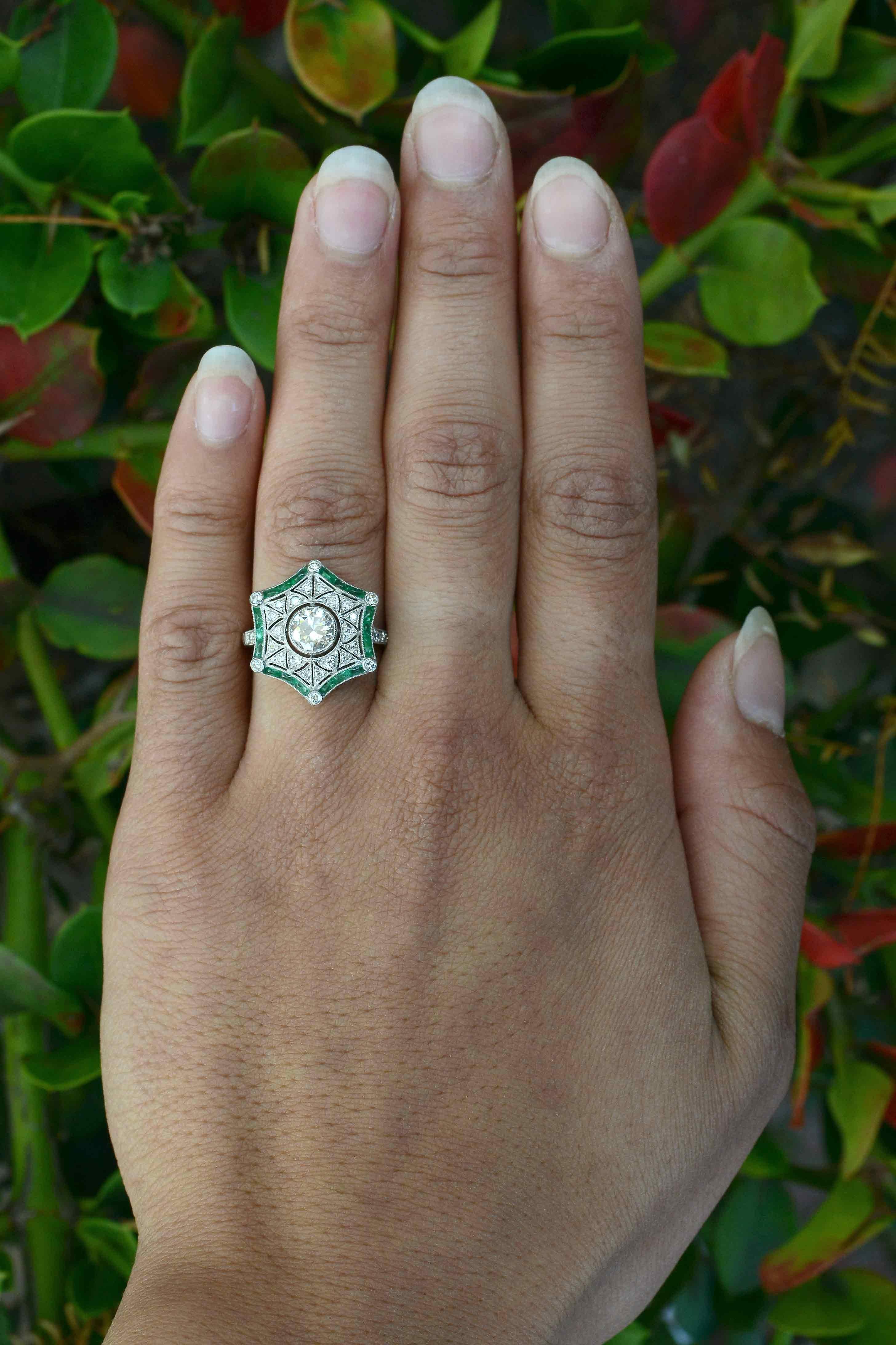 A revivalist Art Deco Style diamond emerald engagement ring of a fascinating star design. Centered by a bezel set 3/4 carat diamond with a fiery and brilliant scintilllation surrounded by highly detailed filigree openwork accented by lush emerald