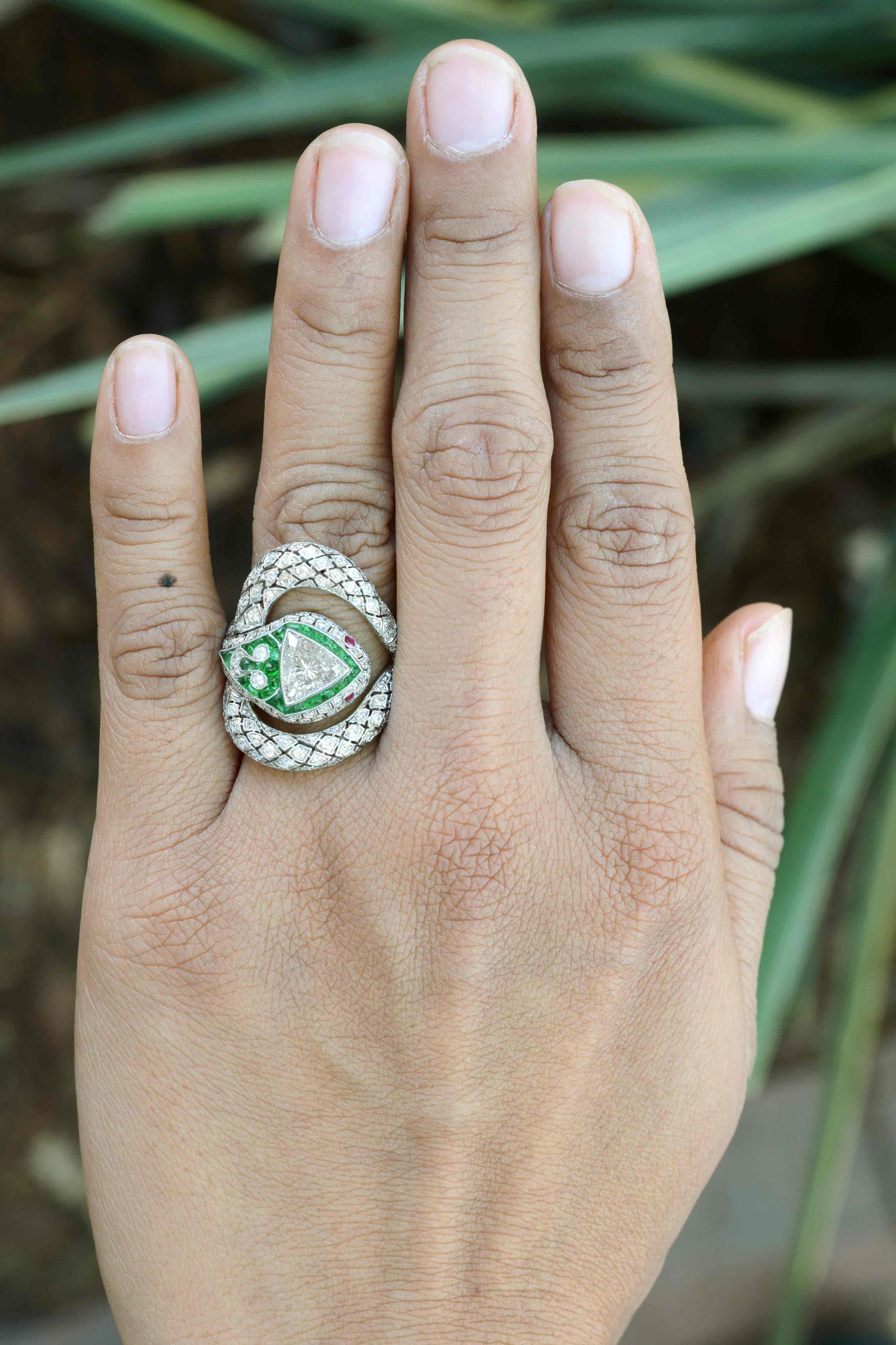 A fabulously elegant and charming Art Deco Style snake ring. Centered by a 1.17 carat triangle diamond (trillion) of a scintillatingly brilliant personality wrapped in lush emeralds, diamond encrusted scales and haunting ruby eyes. This Egyptian