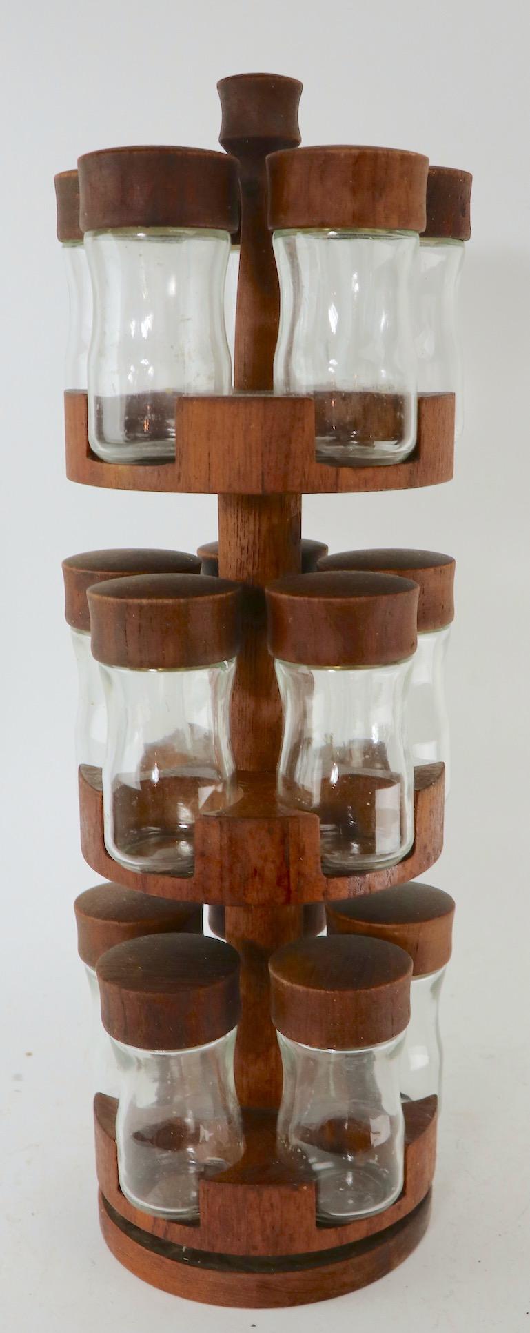Unusual revolving three-tier teak and glass spice rack by Digsmed, Made in Denmark (Danmark). The teak stand has three circular shelves each holding five bottles, total 15 spice bottles. The glass spice jars have different styles of plastic caps, to