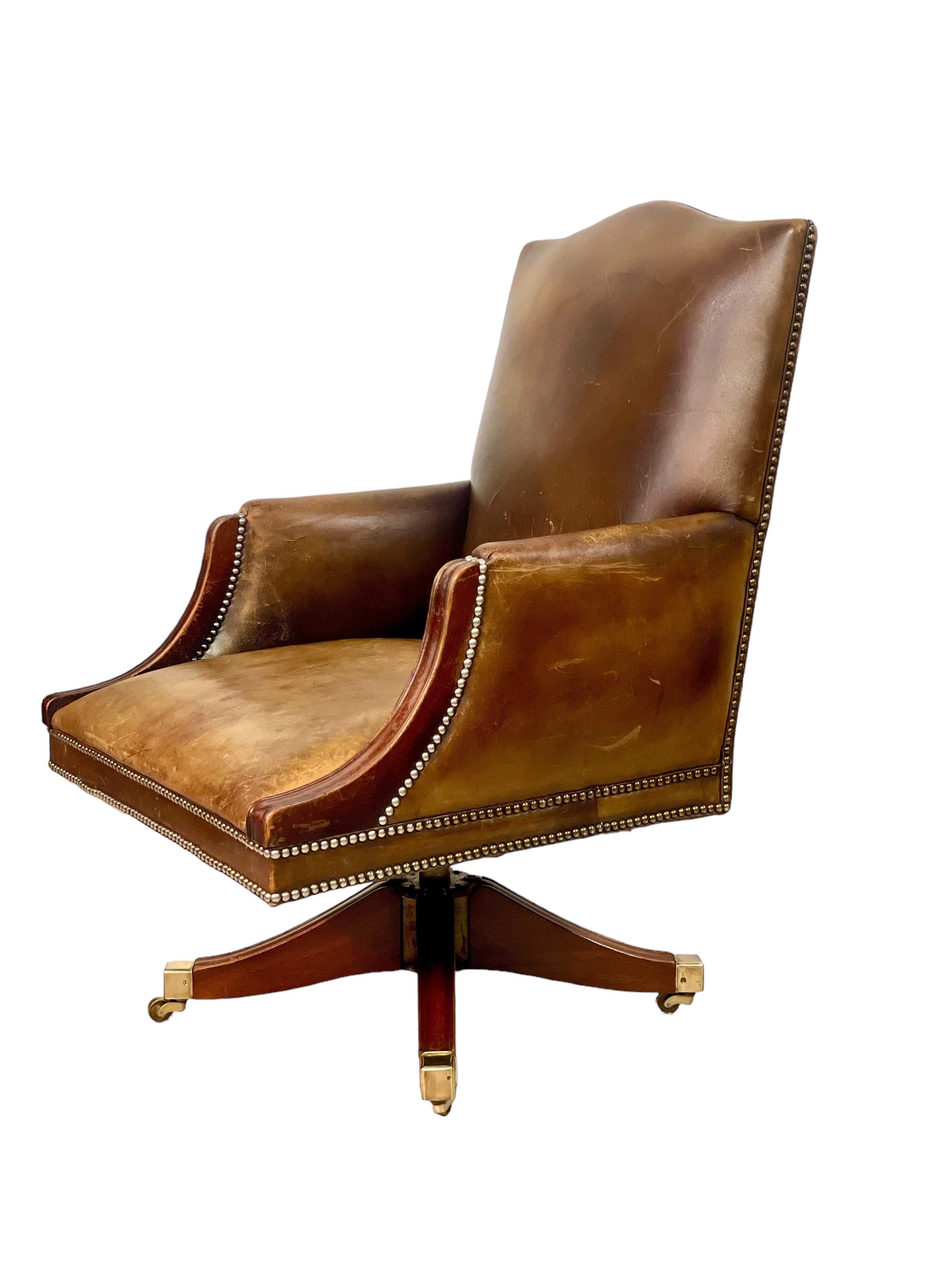 A superb and very handsome revolving leather director's chair with a high back and comfortably wide, padded seat. The arm rests are shaped and enclosed, and the leatherwork nicely aged and full of timeworn character, and accented with brass nailhead