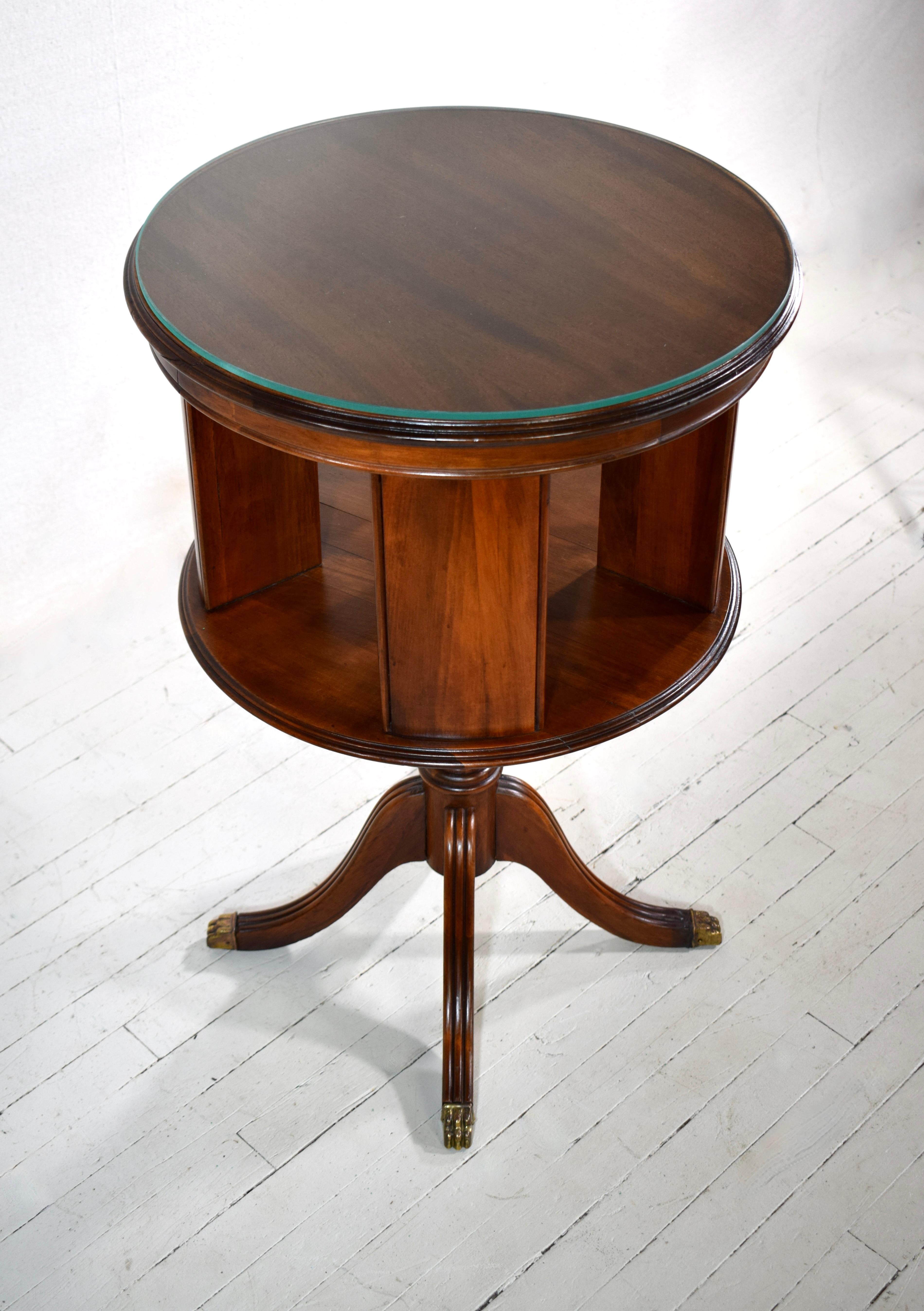 Early 20th c. English Neoclassical revolving Mahogany side drum table featuring book case cubbies on a pedestal base with brass paw feet & custom glass top. The sweet smaller size is suitable for versatile placement & use.