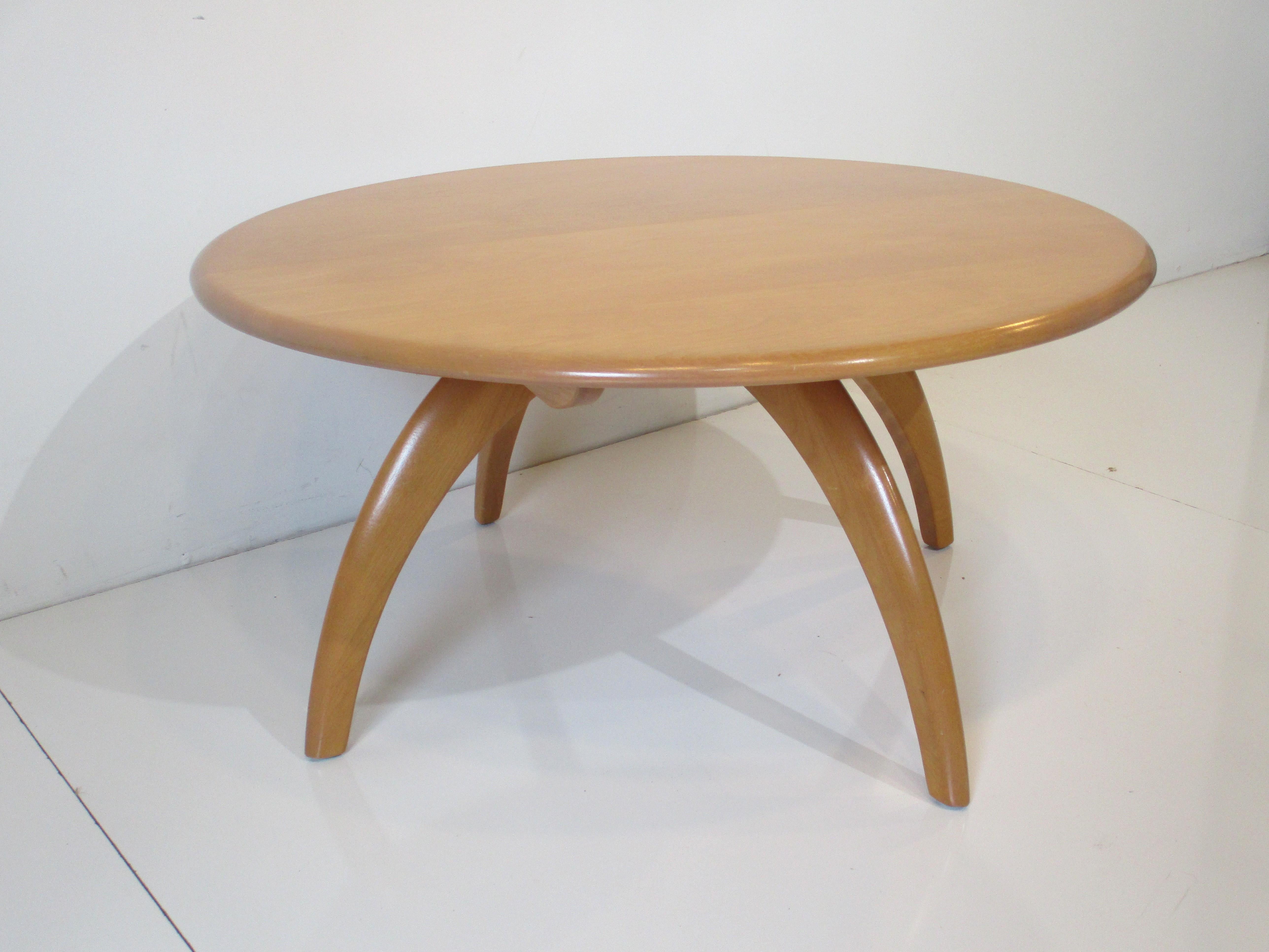 A solid maple wood round coffee table with revolving top in the champagne finish with sculptural curved legs. A timeless design of simplicity and function by Leo Jiranek and Ernest Herrmann for the Heywood Wakefield furniture company model # M306G