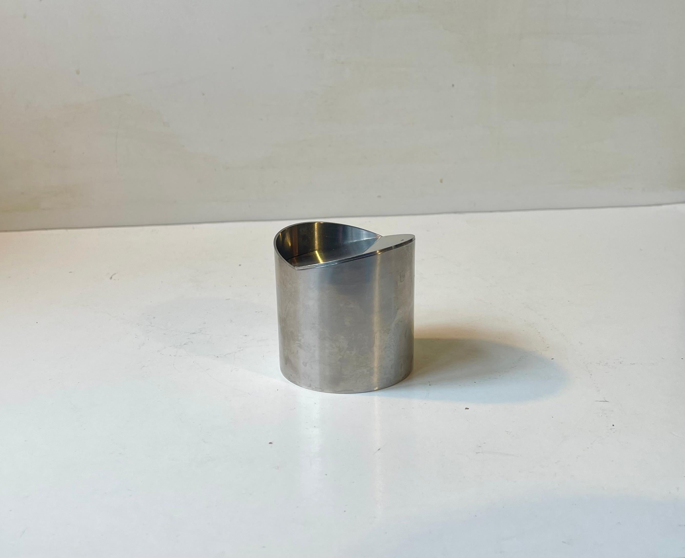 A stylish stainless steel ashtray designed by Roelandt and manufactured by Stelton in Denmark during the 1980s. Similar to Arne Jacobsen's cylinda-line but with a tilting/revolving mechanism/lid instead. Imprinted with designer and makers marks