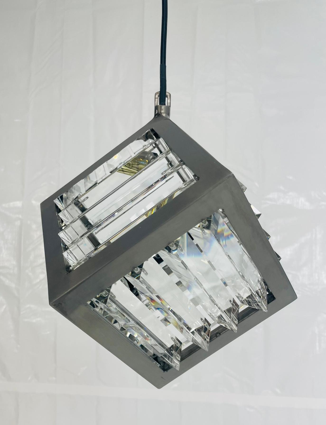 Il pendente è caratterizzato da una forma cubica realizzata in acciaio naturale, con pannelli di vetro ottico tagliato con precisione che rifrangono la luce in drammatici motivi prismatici. La sua struttura geometrica pulita rivela un gioco