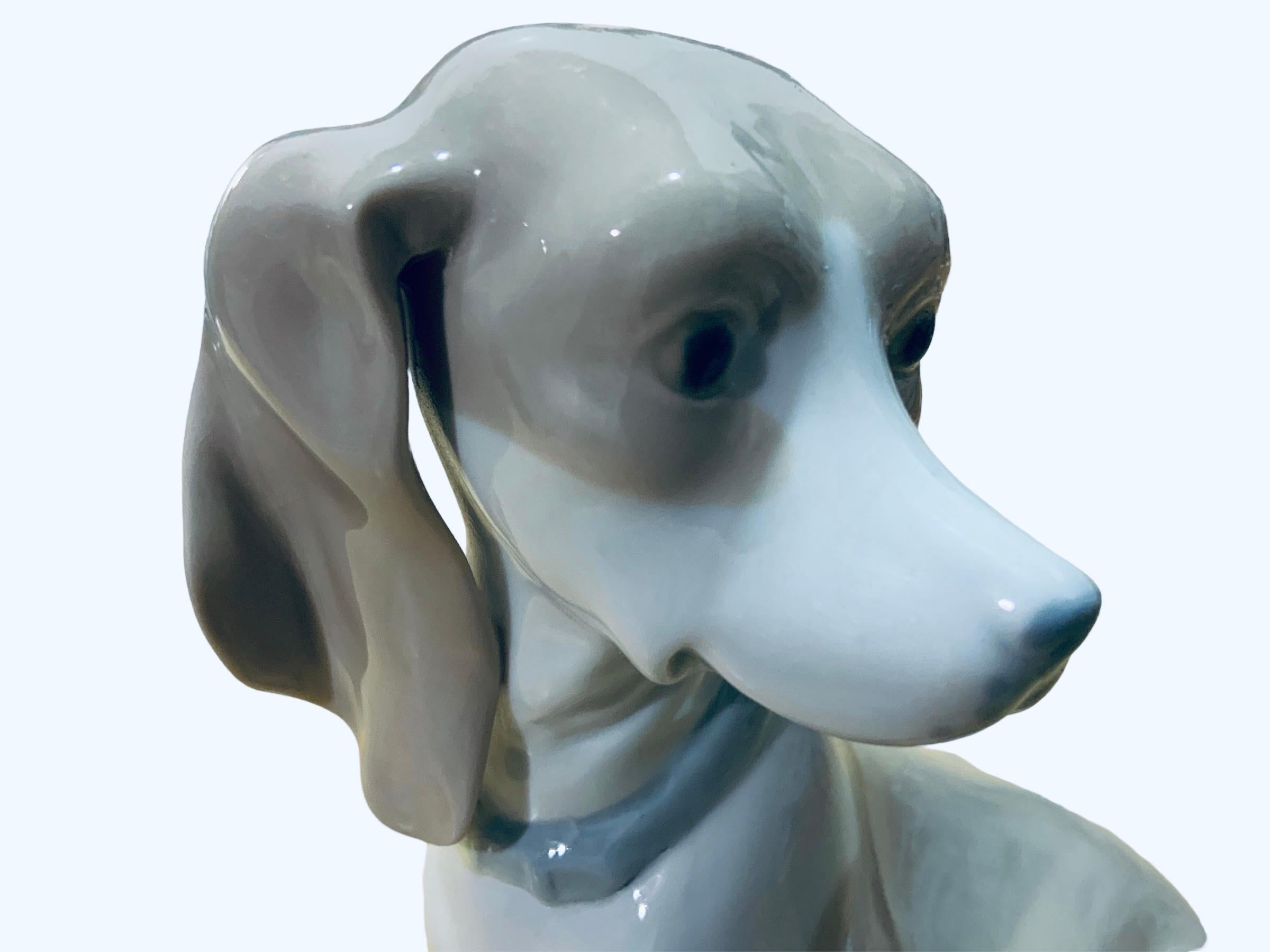 This is a Rex Valencia porcelain figurine of a dog. It depicts a hand painted adorable Hummelwerk dog standing up with a blue belt in his neck and full of white and brown hair. The Rex Valencia hallmark is below the figurine.
