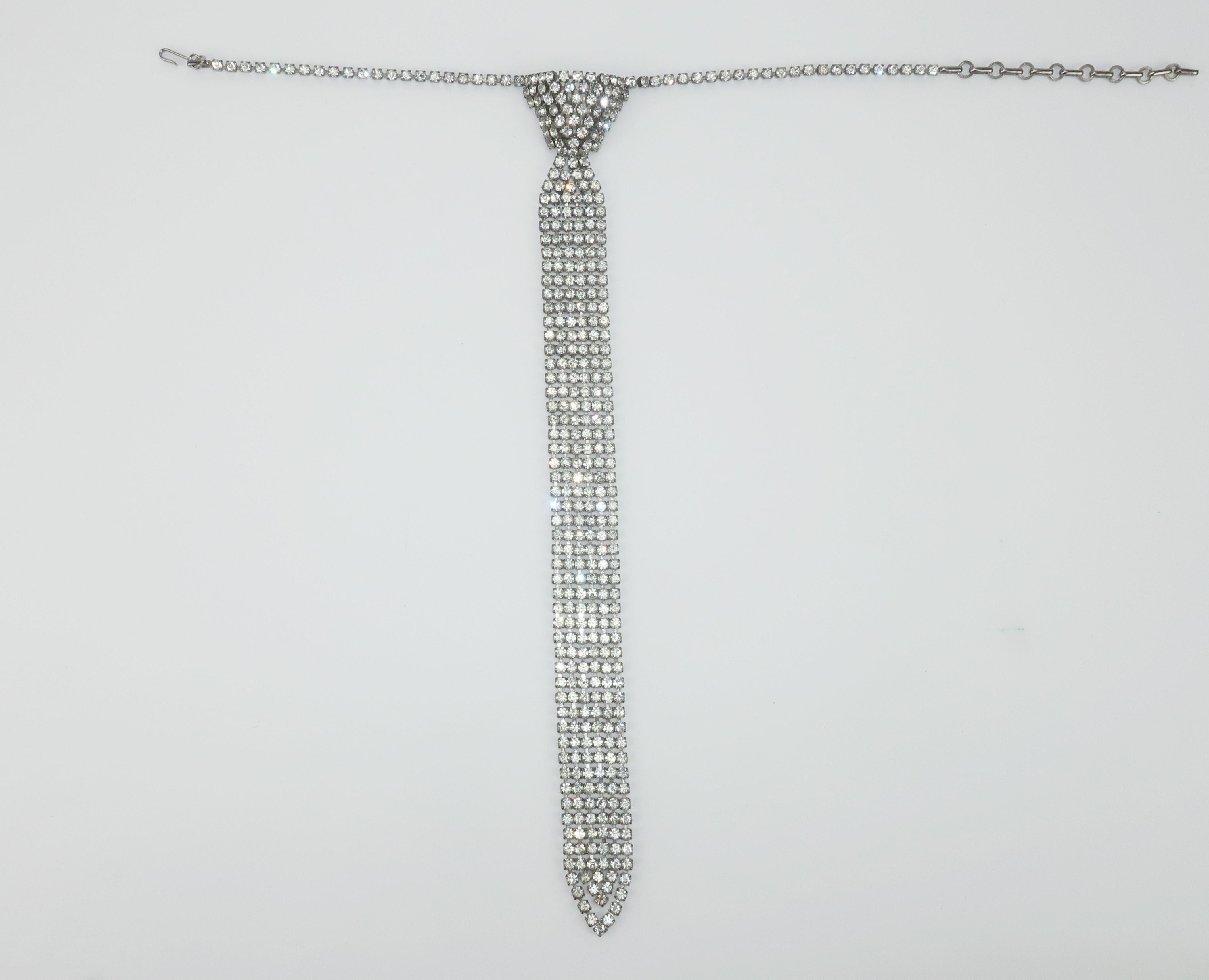 1970's disco glam rhinestone necklace in the whimsical shape of a knotted necktie.  The ultra sparkly stones draw the eye to the neck line and can serve to accent a collared shirt or a plunging décolleté.  The adjustable hook and chain allows for a
