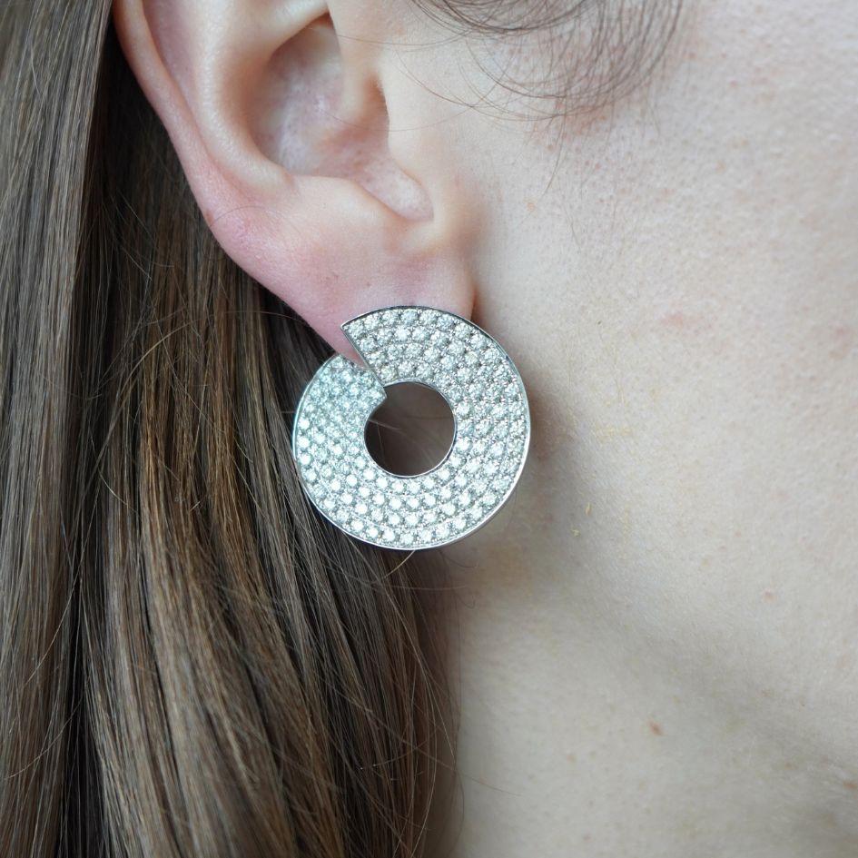 Questo paio di orecchini in oro bianco 14k placcato in rodio presenta una sorprendente silhouette circolare con un taglio geometrico in alto al centro. Crea un interesse visivo quando un'estremità del cerchio si infila dietro il lobo dell'orecchio.