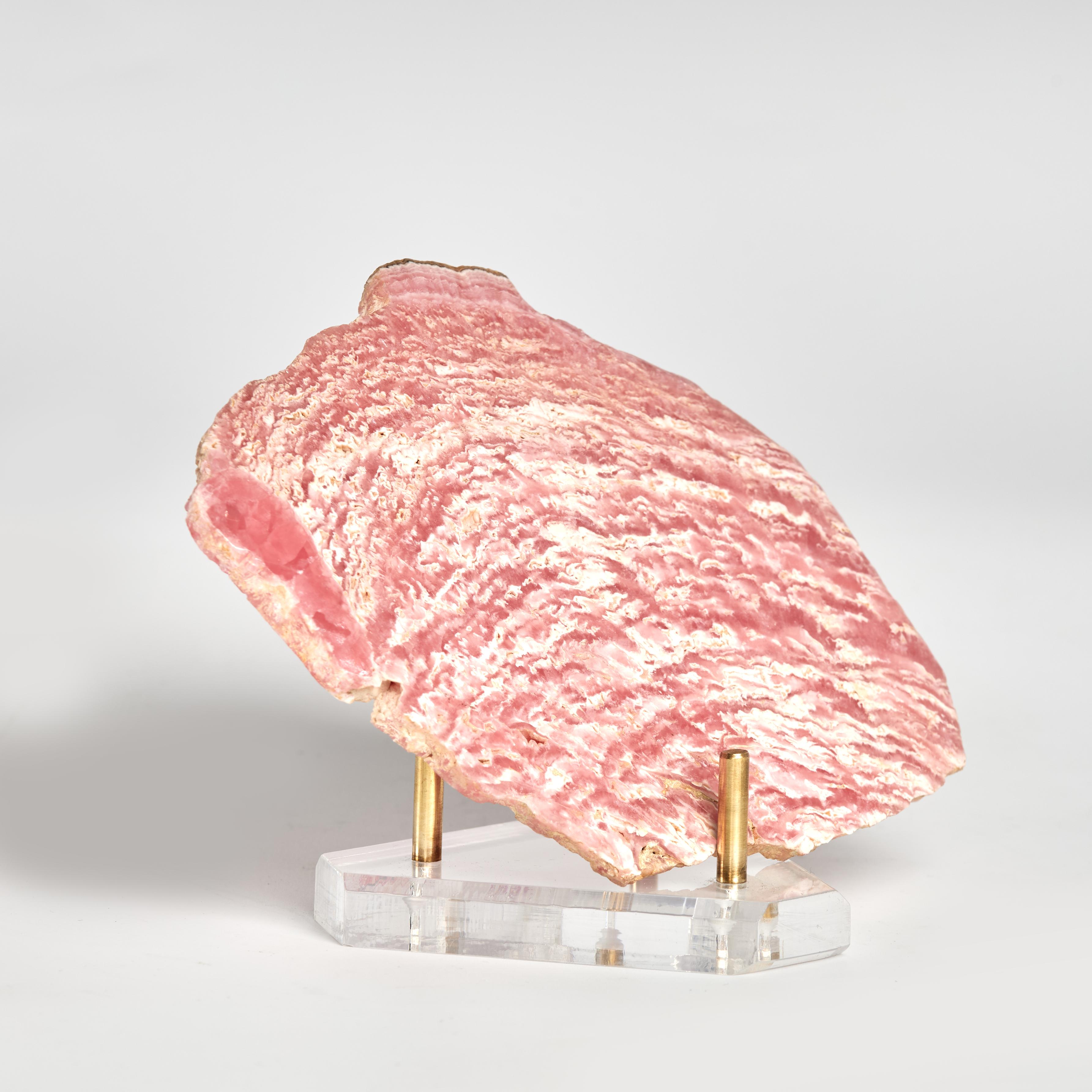 Llamativa rodaja tallada y pulida de rodocrosita, un mineral semiprecioso, con su característico color rojo y bandas blancas. Se presenta en un soporte personalizado de lucita y latón.