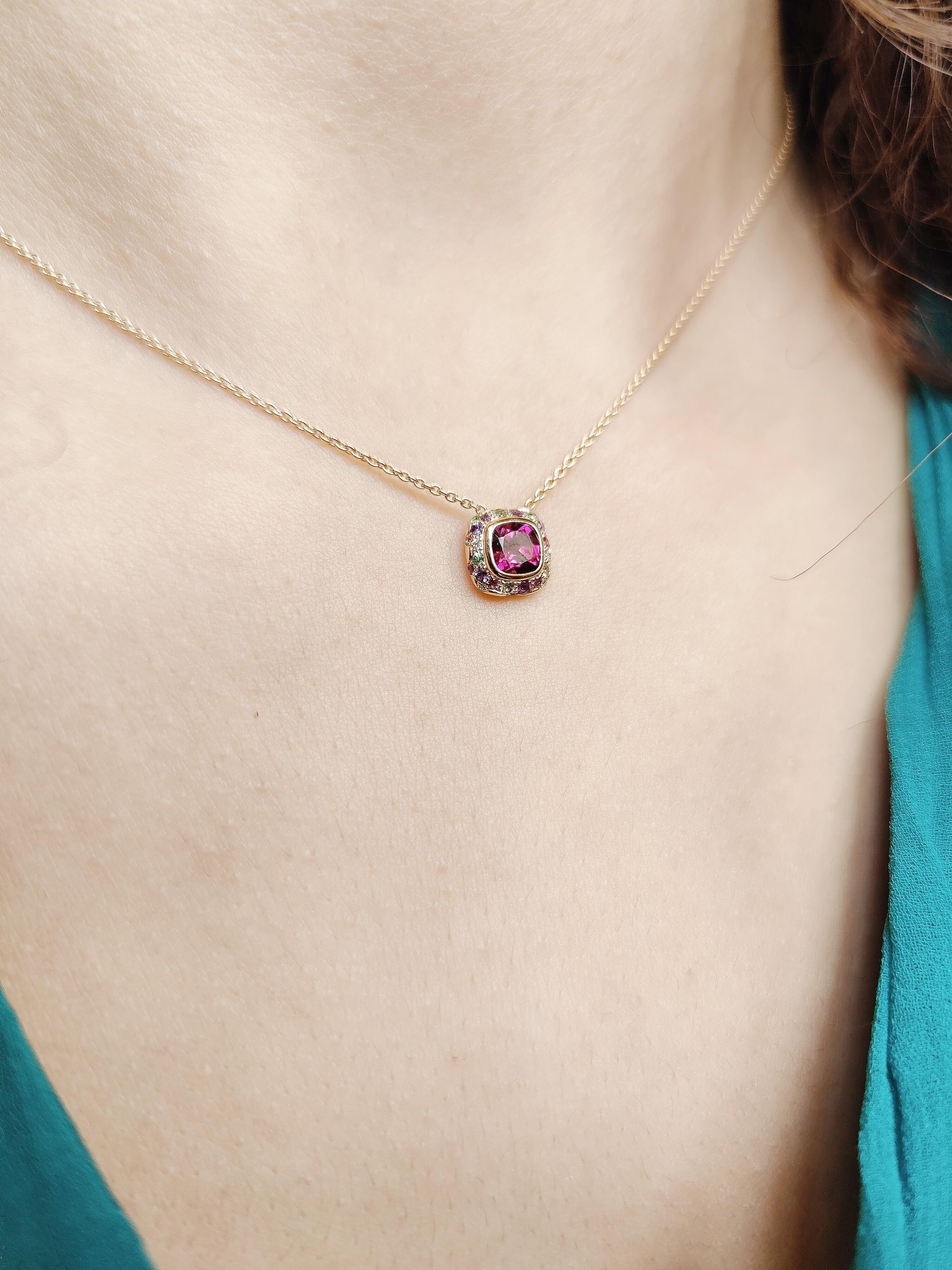  A blend of deep pink and red with a hint of purple is what makes the rhodolite garnet appear so extraordinary and desirable. 

This rhodolite is cushion cut and mounted in 18 karat rose gold in a bezel setting. Around are set a mix of tsavorite,