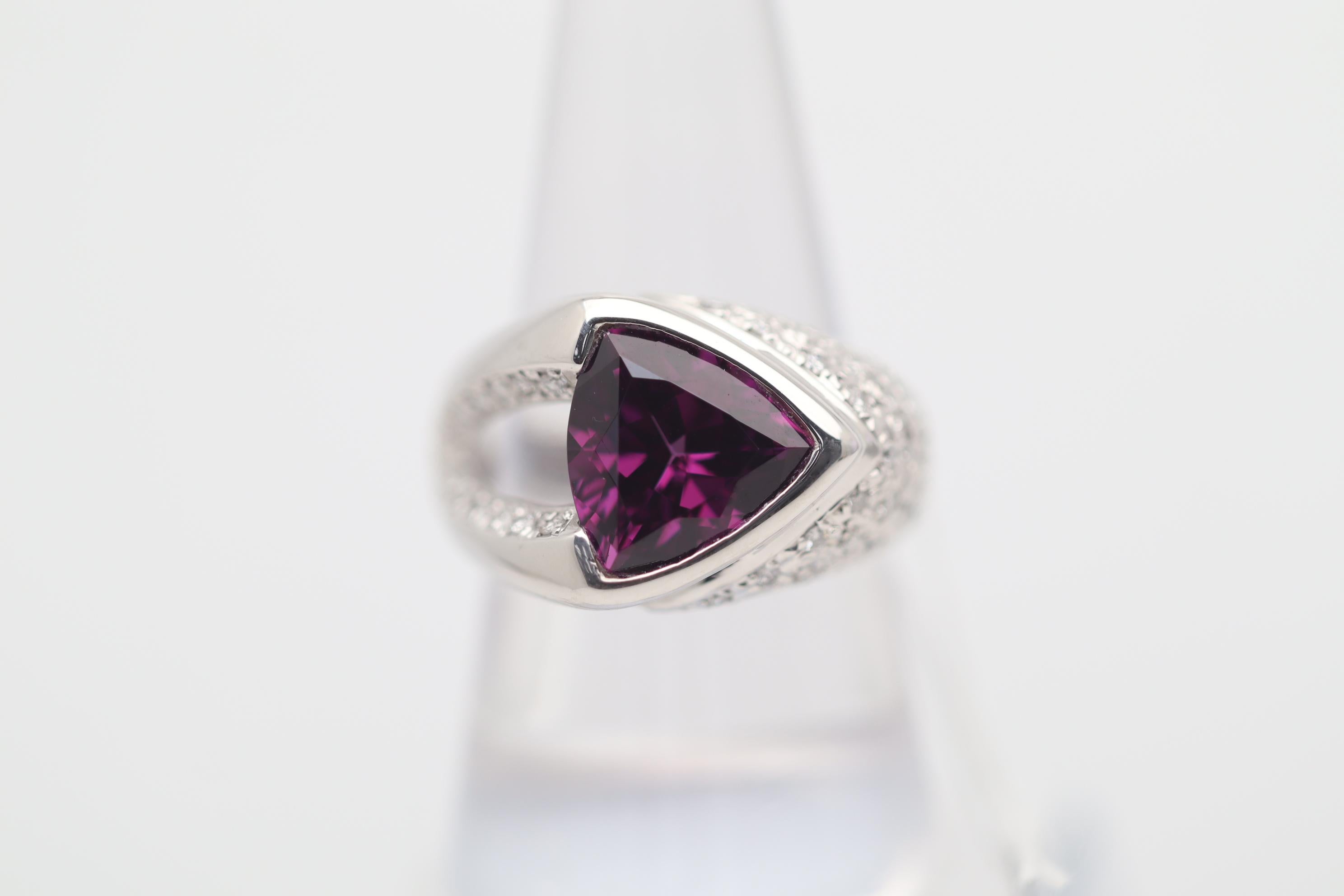 A unique ring featuring a 4.85 carat rhodolite garnet, which has a lovely triangular shape and intense vivid purple-red color. It is complemented by 0.36 carats of round brilliant-cut diamonds set around the ring. Hand-fabricated in platinum and