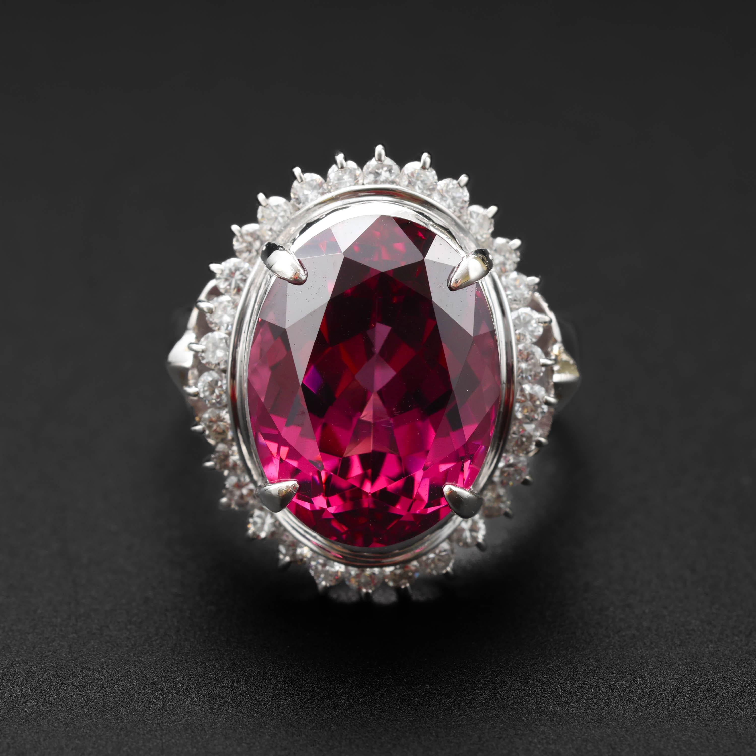 This impressive ring features an oval-cut 9.78-carat natural vibrant raspberry rhodolite garnet, surrounded by a halo of brilliant-cut diamonds that total .59  carats. The ring is rendered in platinum and bears the unidentified maker's mark of its