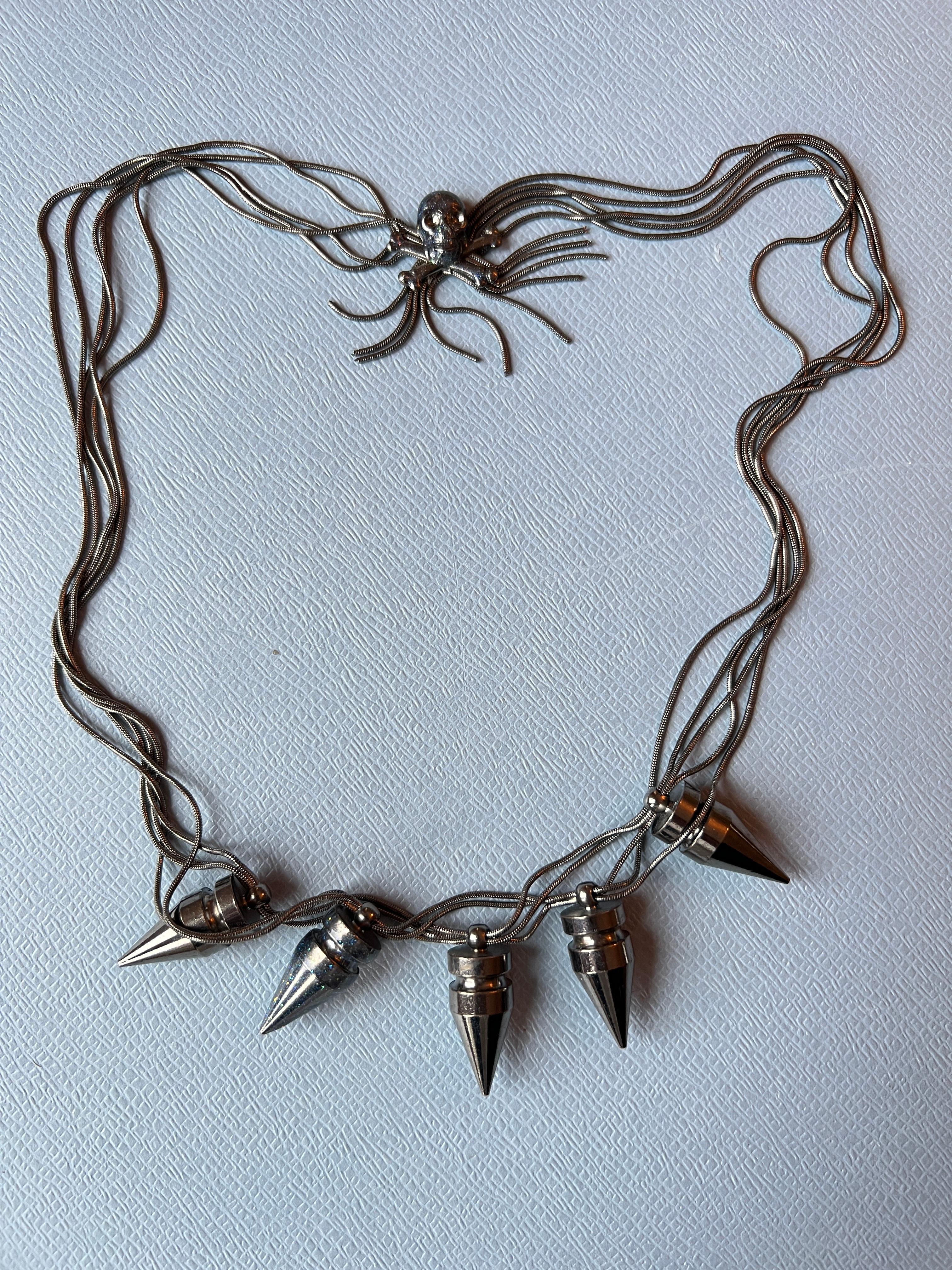 Collana con catena di borchie con diverse borchie in vetro smaltato dipinte a mano in blu e un motivo di teschio e ossa sul retro. Realizzato in ottone con un rivestimento di rutenio scuro  placcatura (