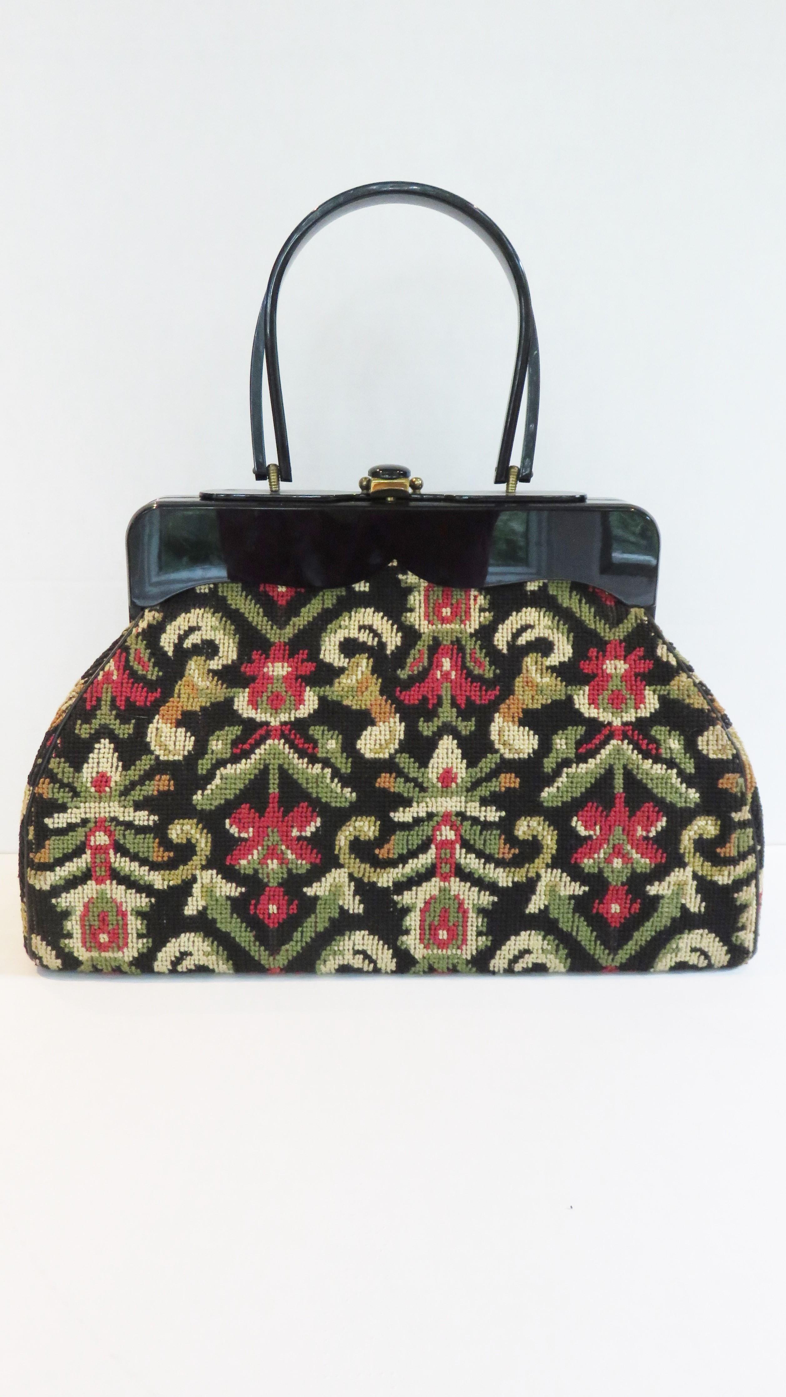 A gorgeous large needlepoint handbag in a green, yellow and red abstract pattern on a black background. It has a shapely black Lucite frame, double rounded top handles, and gold clasp with a black button. It is silk lined with 2 inner