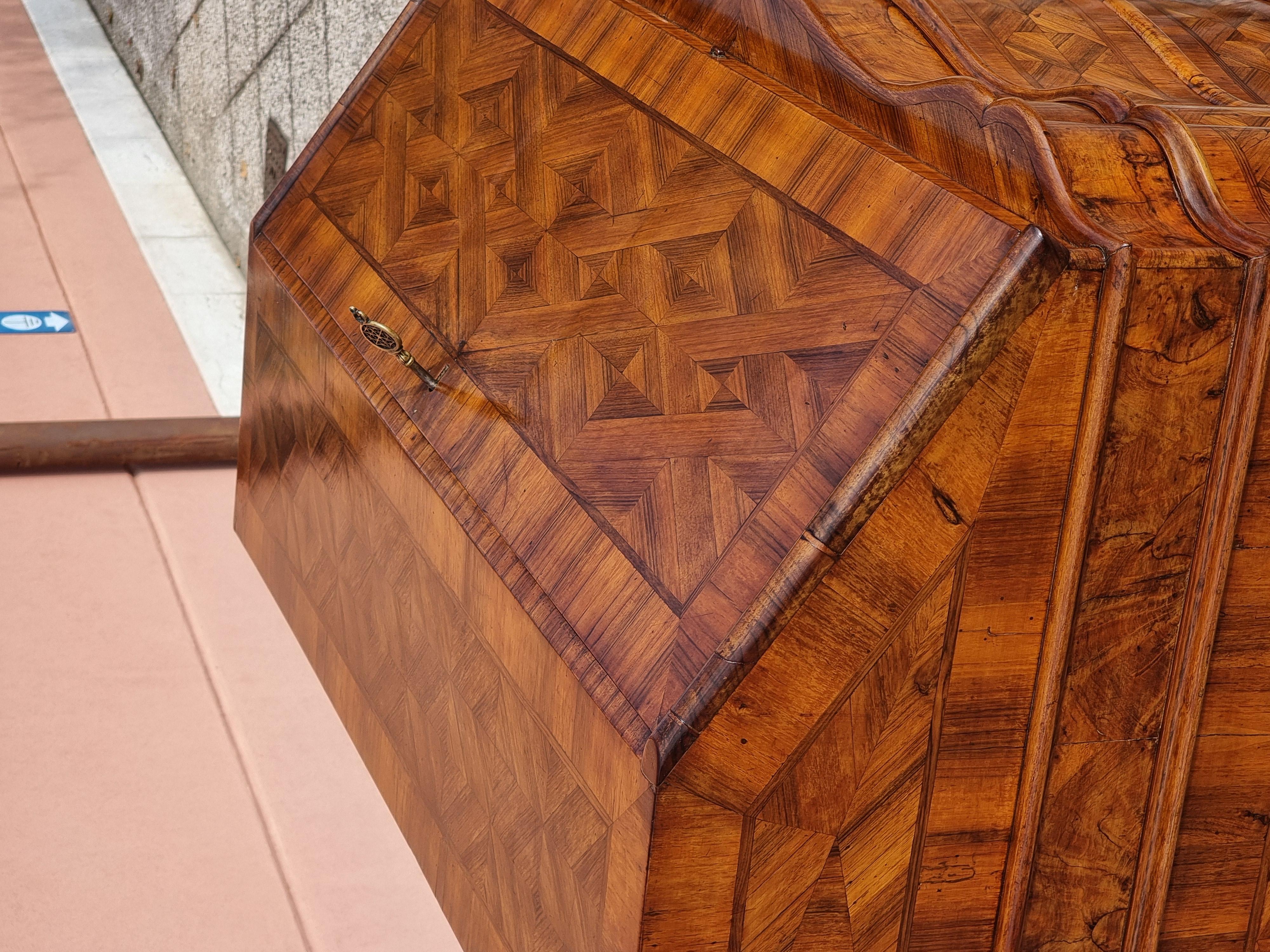 Elegante ribalta veneta della prima metà del Settecento, interamente lastronata e intarsiata in noce e radica di noce, con raffinati motivi geometrici continui su fronte e fianchi. Il fronte mosso presenta tre grandi cassetti sagomati, arricchiti da