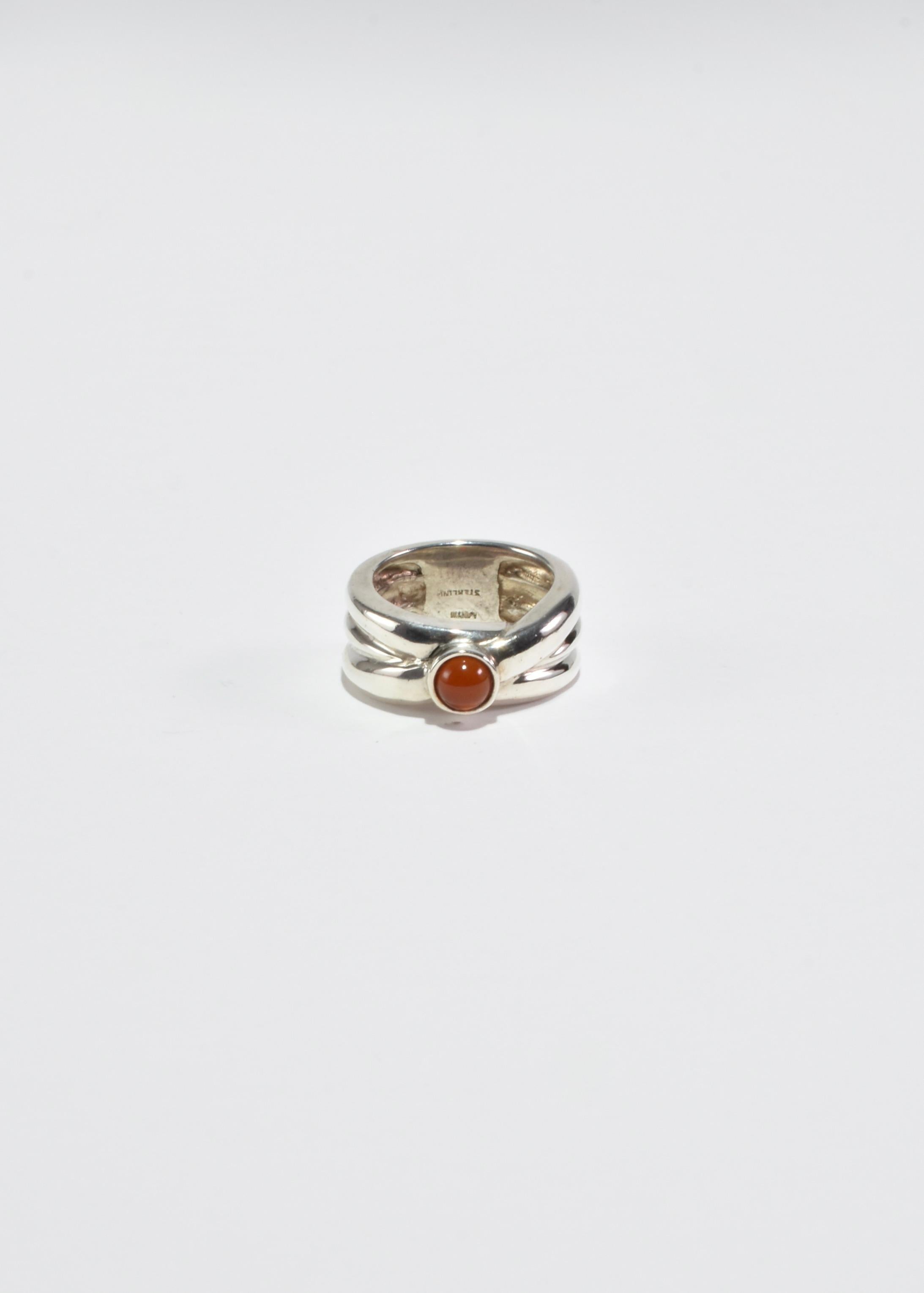 Vintage silver ring with a round carnelian cabochon and ribbed detail. Stamped Sterling.

Material: Sterling silver, carnelian.