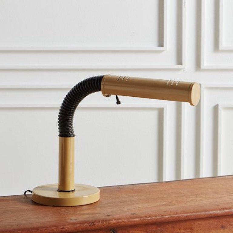 A vintage gooseneck desk lamp featuring a round mustard yellow metal base and shade. This lamp has an adjustable black ribbed plastic neck which allows the light to be directed in a variety of directions.