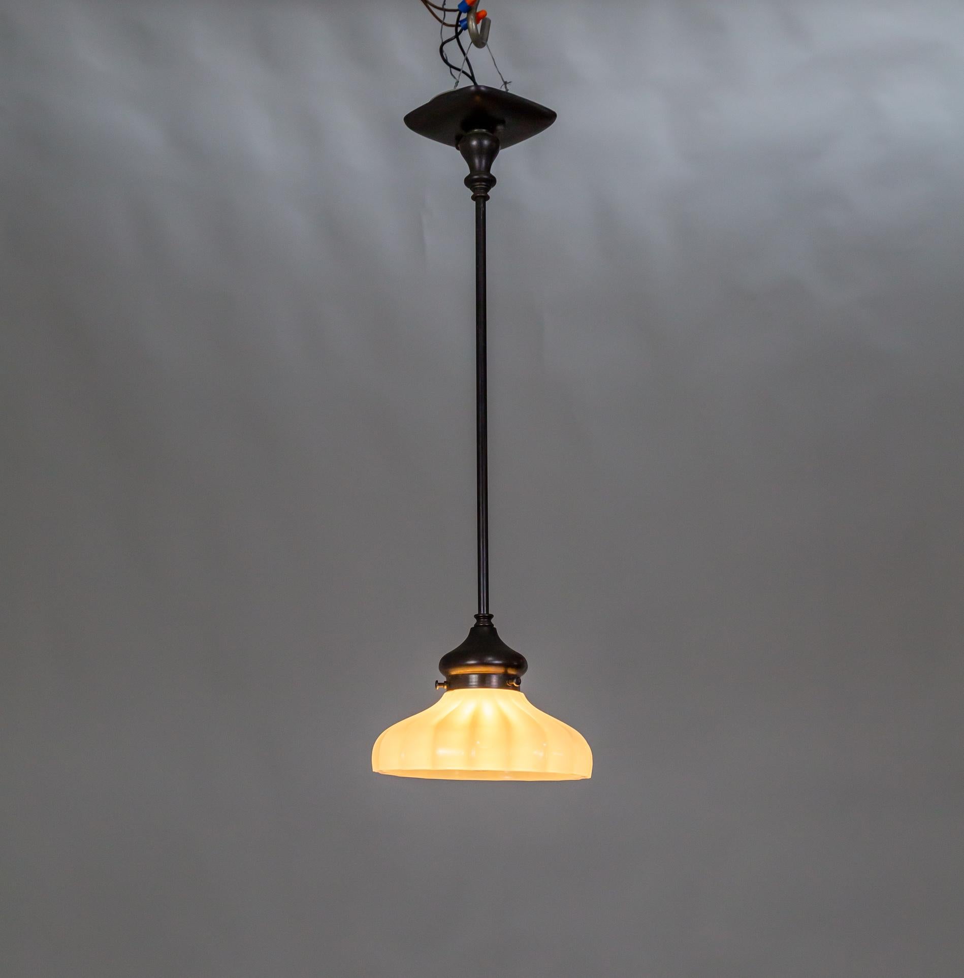 Una lampada a sospensione a stelo nera con paralume in vetro opalino rigato e baldacchino quadrato dai bordi arrotondati. Vetro dei primi del '900 e gambo in ottone antico e verniciato. Può contenere una lampadina media. 23,5