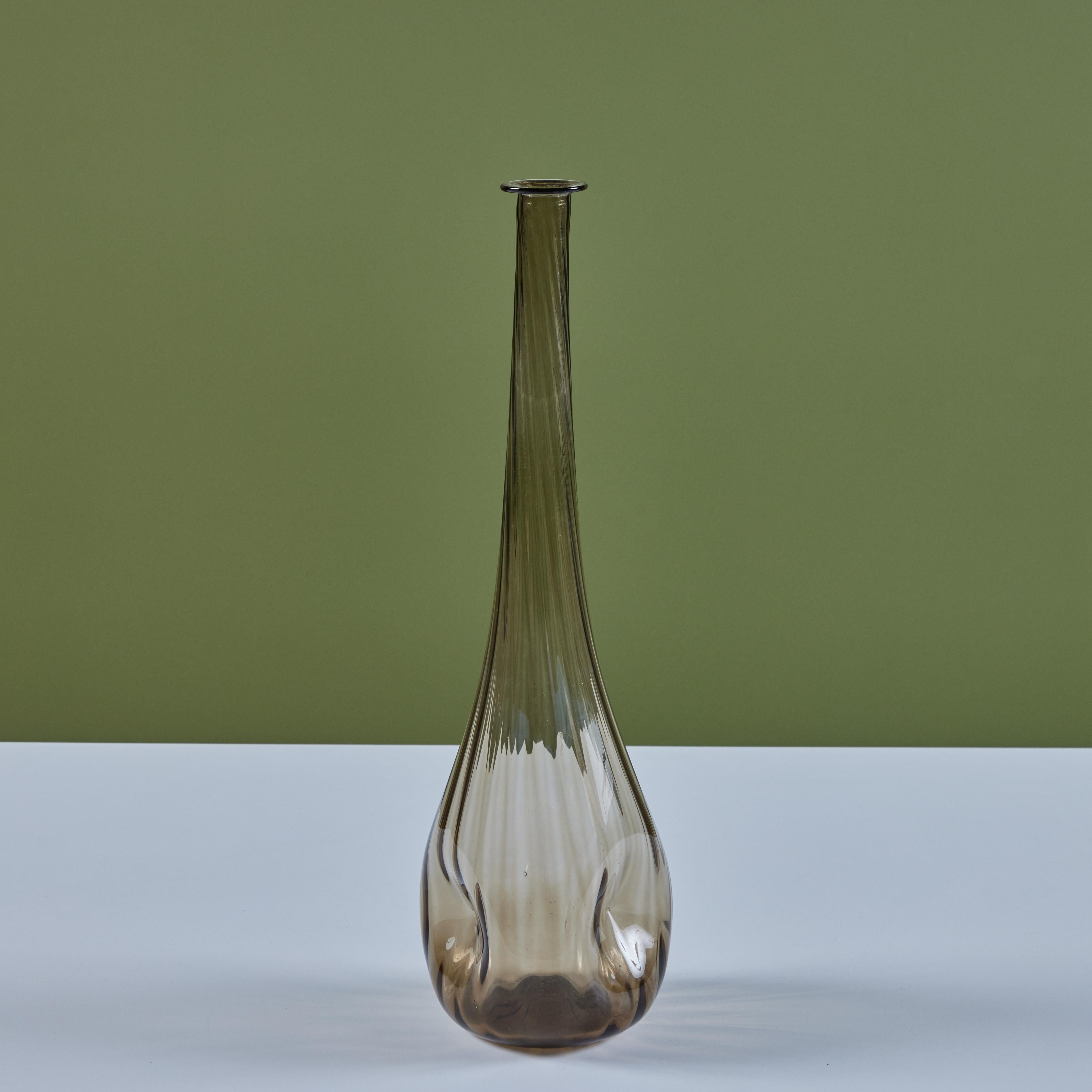 Tall smoked glass vessel or decanter. This piece features a smoked blown glass vessel with rounded bottom and slender neck. The glass has an all over ribbing that spirals at the neck with three dimples around the sides of the glass