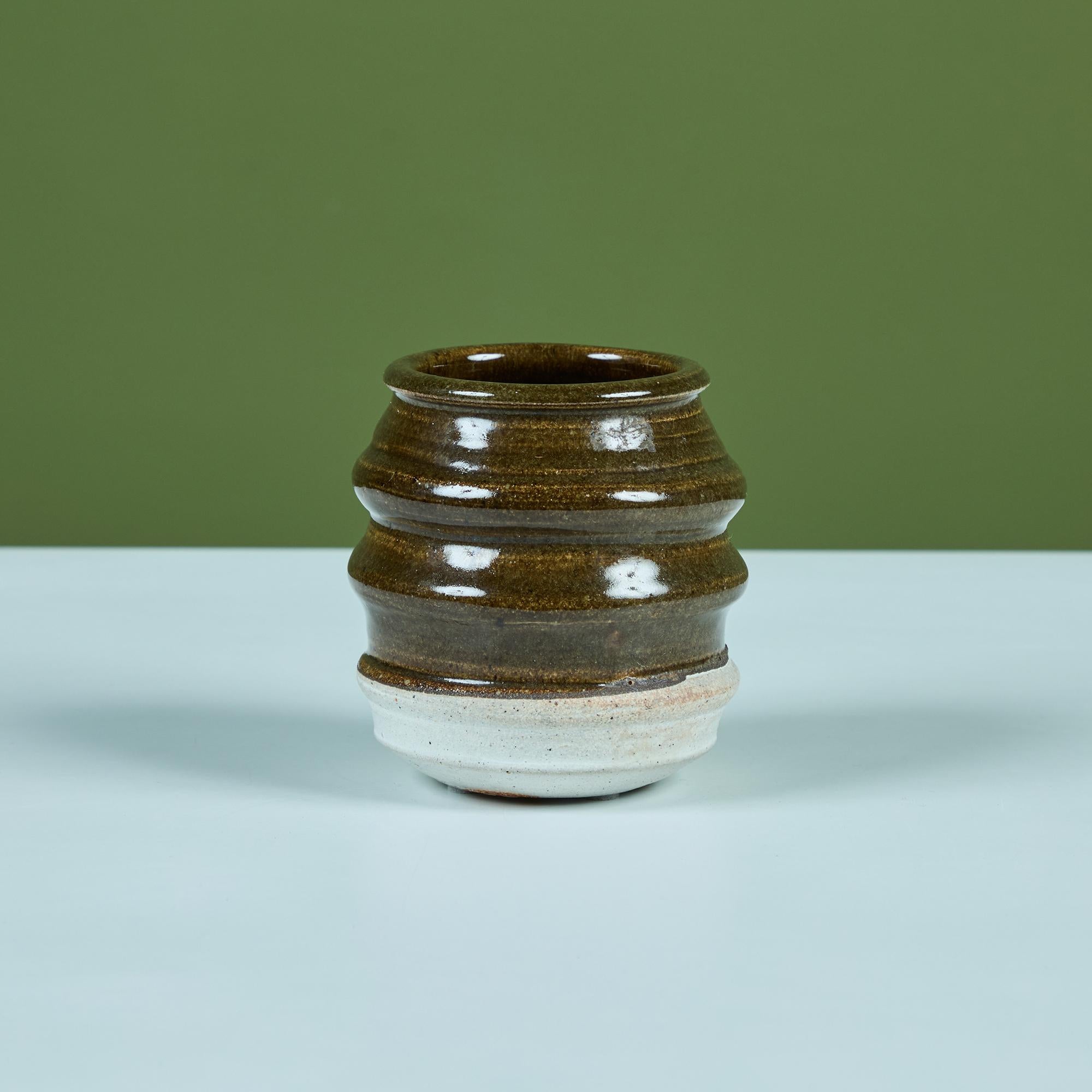 Kleine Tasse aus Studio-Keramik mit geripptem Körper und zweifarbiger Glasur. Die obere Hälfte und das Innere sind in einem glänzenden Olivgrün glasiert, während der Boden des Gefäßes in einem matten Weiß gehalten ist. Signiert vom